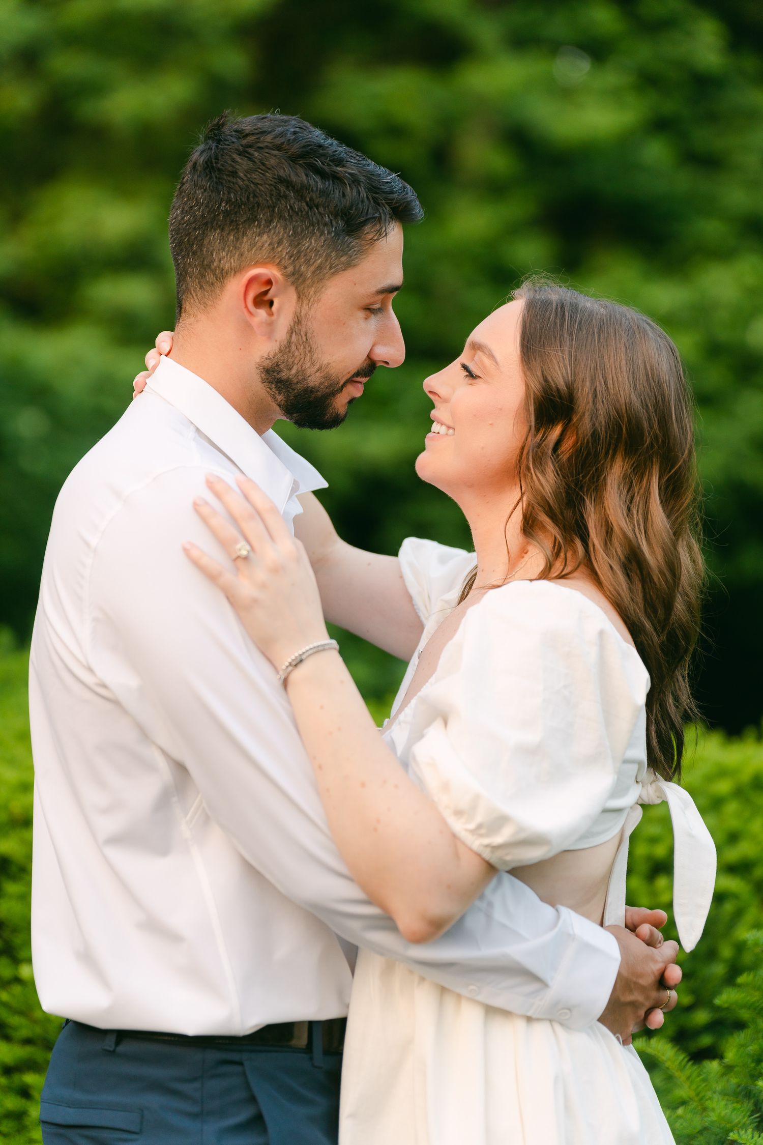 Couple in light summer attire shares a tender moment in a lush garden setting.