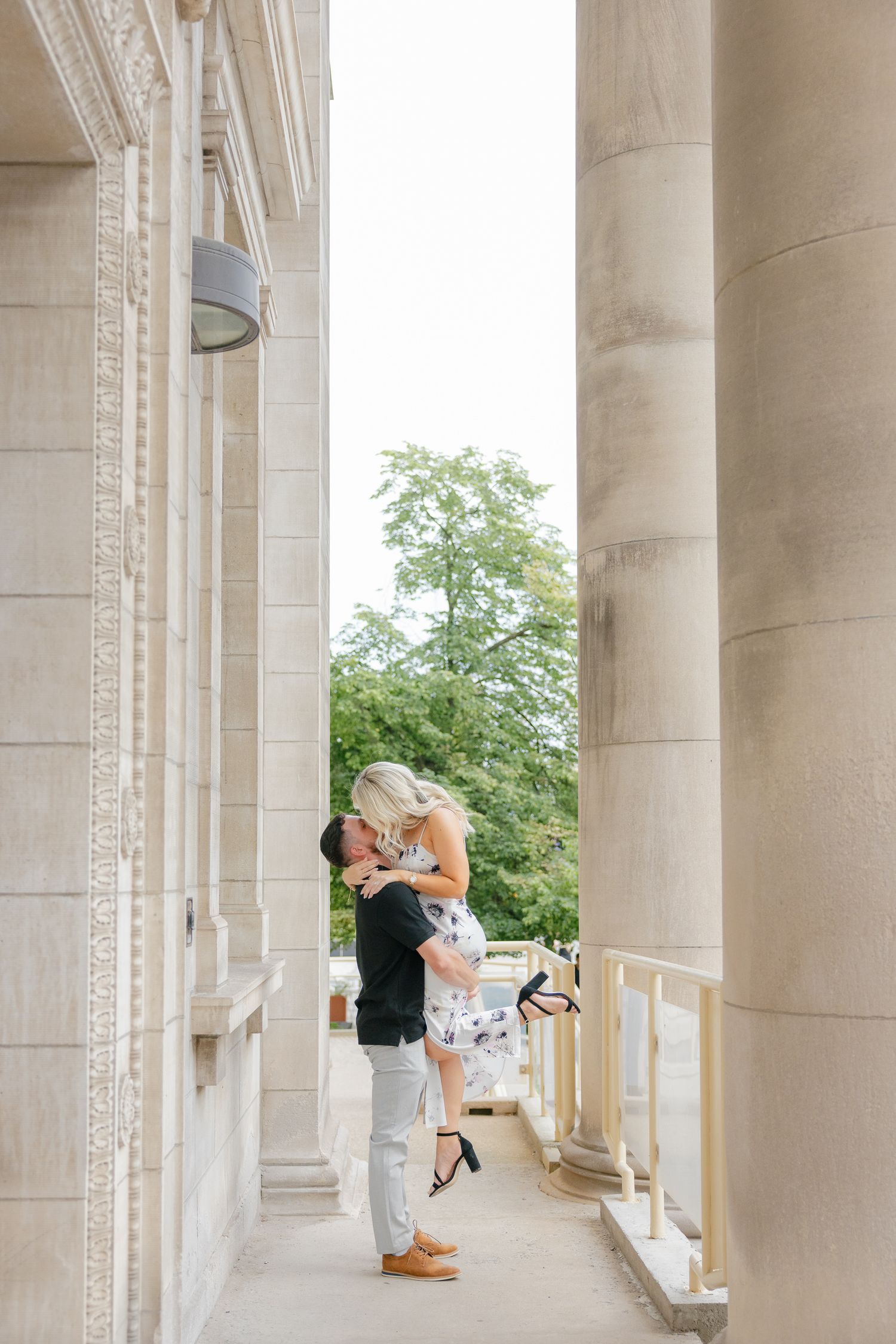 A joyful couple creates a romantic lift pose between classical columns.