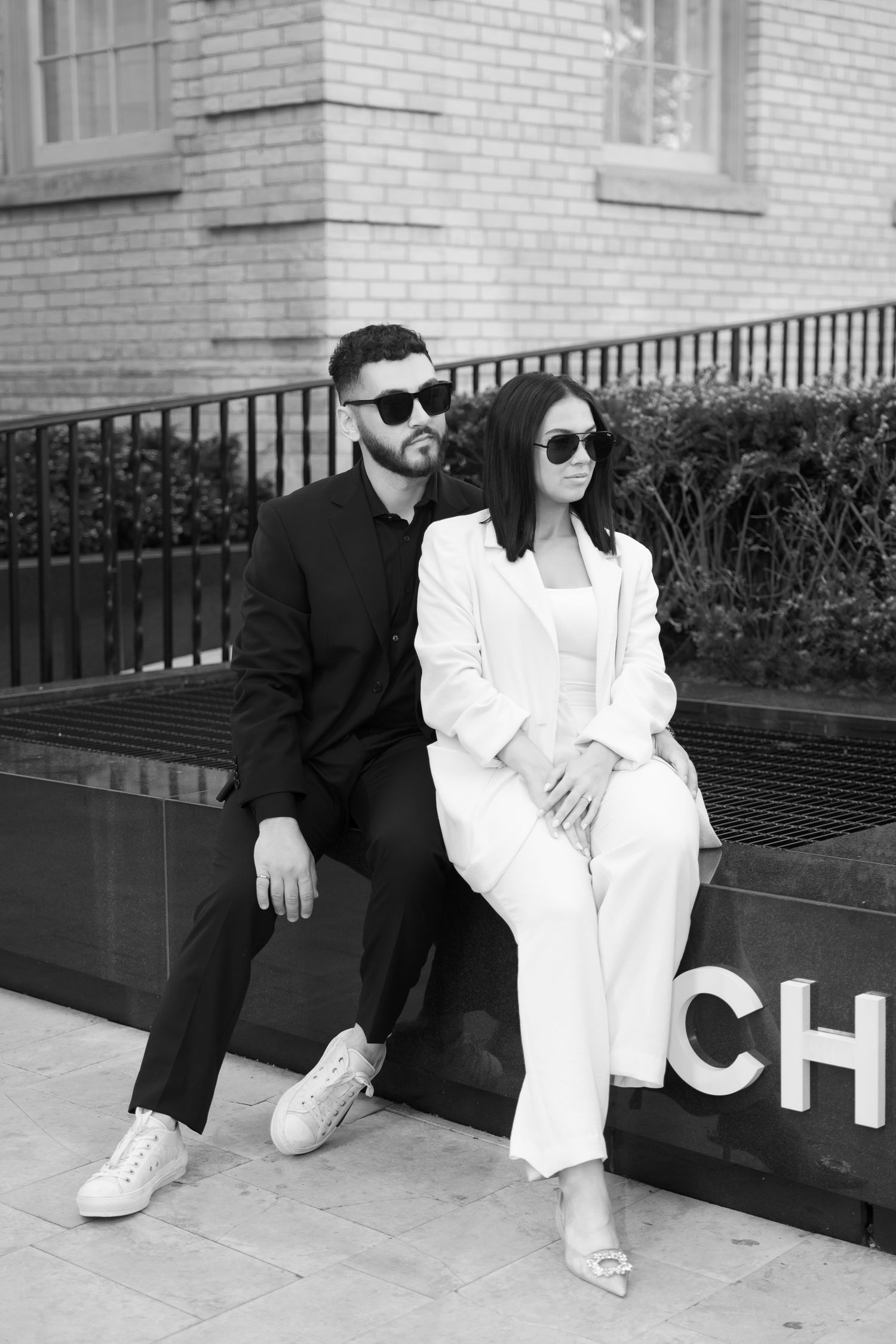 Black and white portrait of couple in contrasting outfits at Chanel boutique entrance.