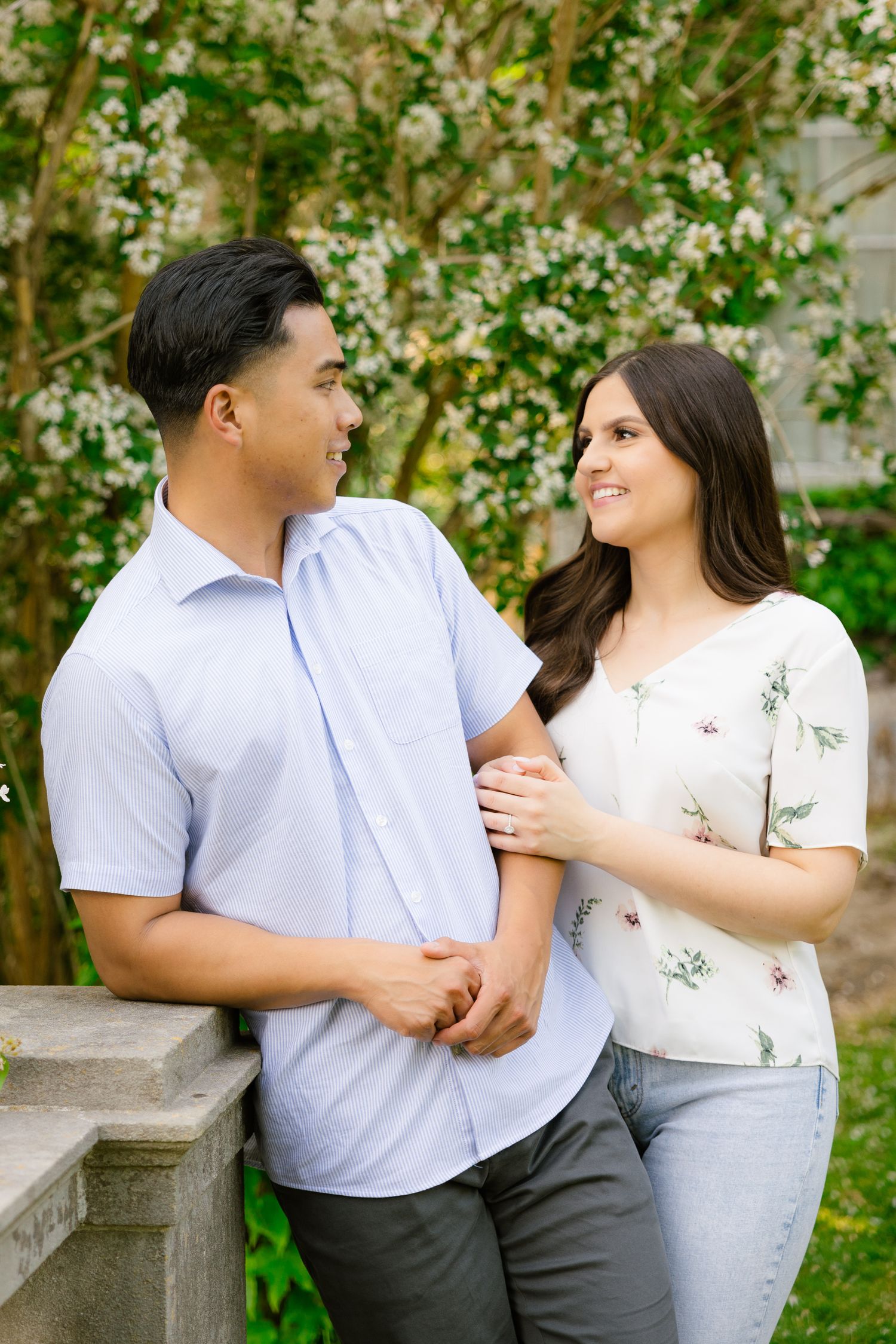 Couple in coordinating white and blue outfits pose against flowering trees in garden setting.