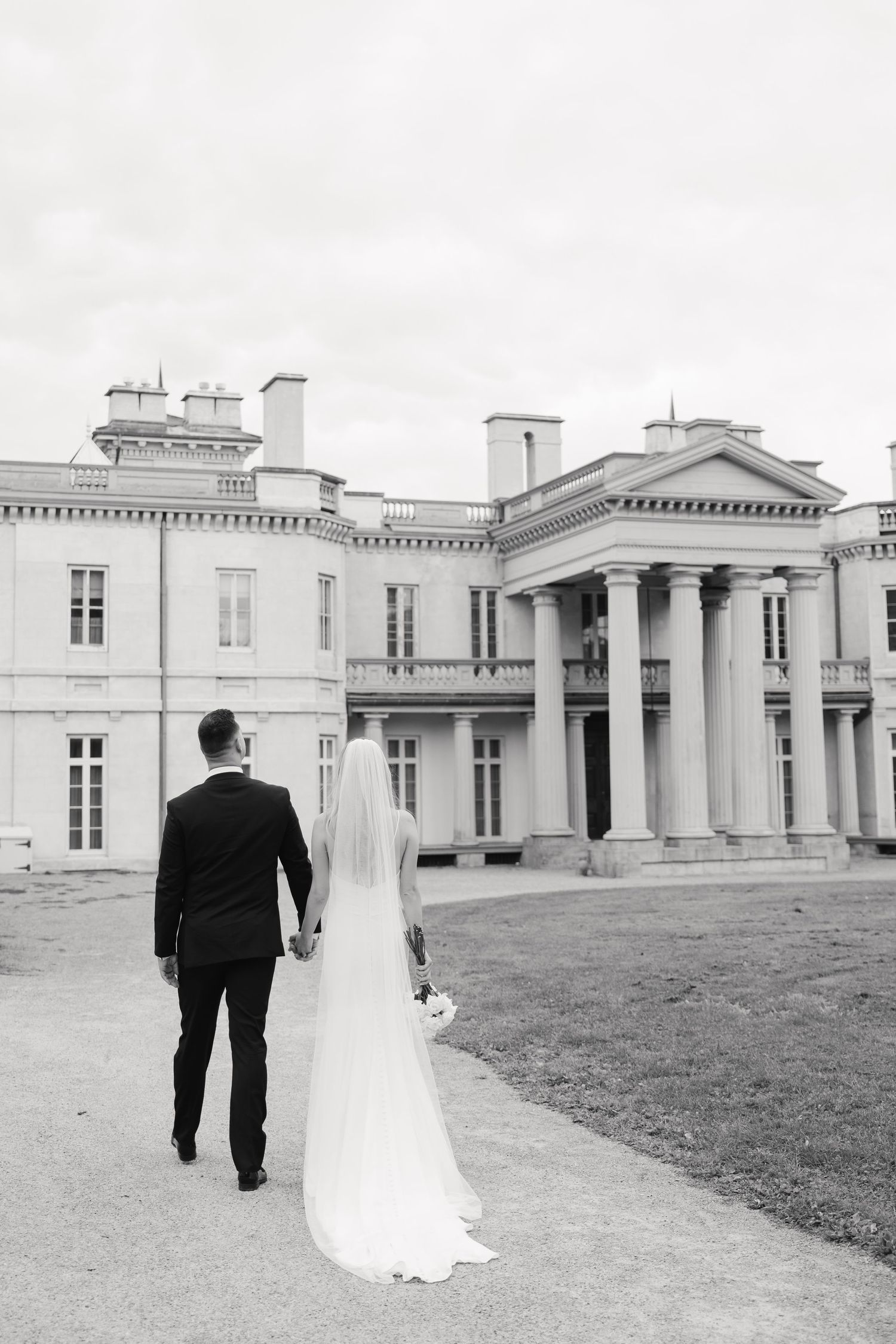 Black and white photo of couple walking towards elegant historic mansion.