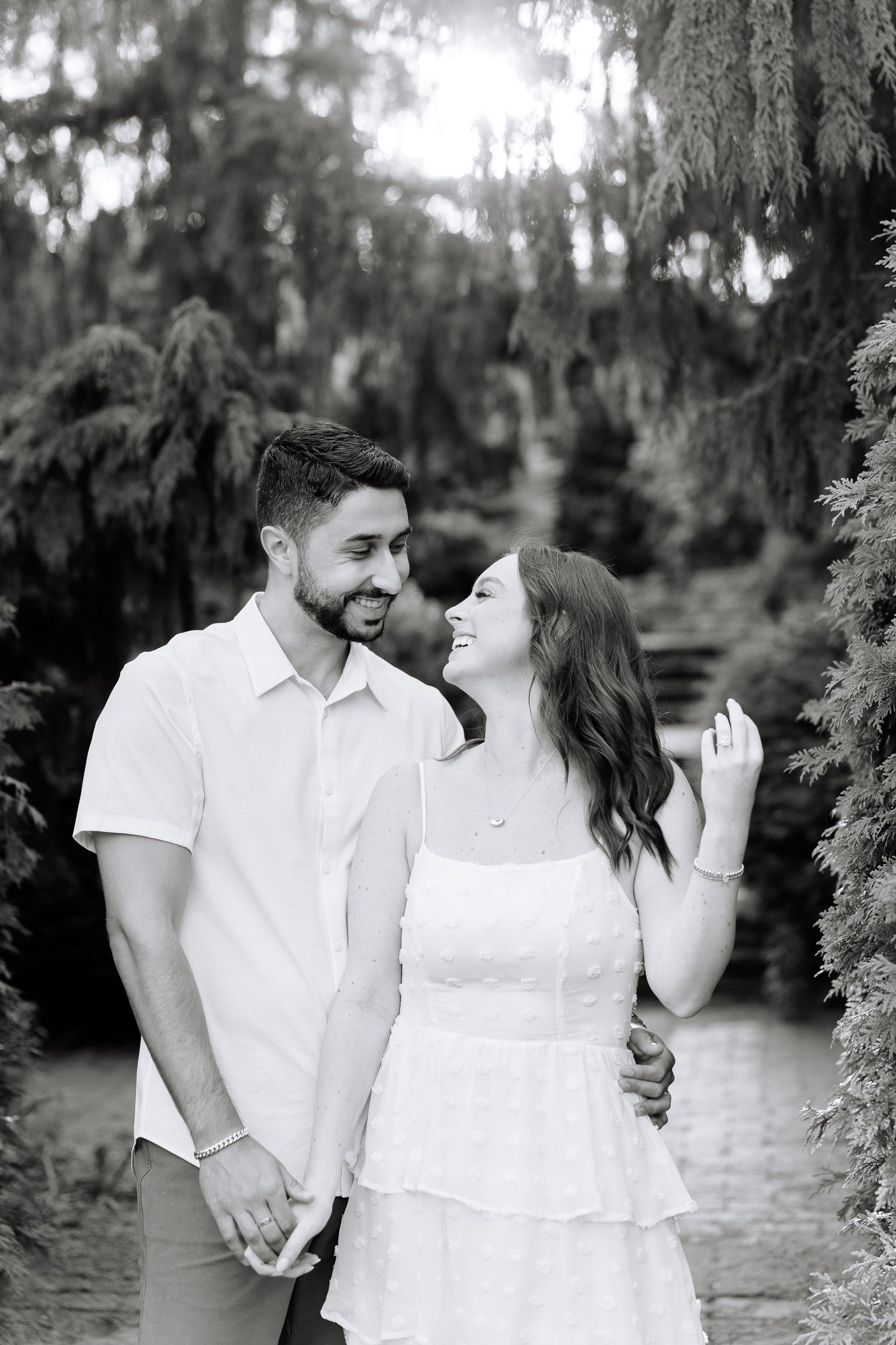 Black and white portrait of a couple sharing a joyful moment in a garden setting.