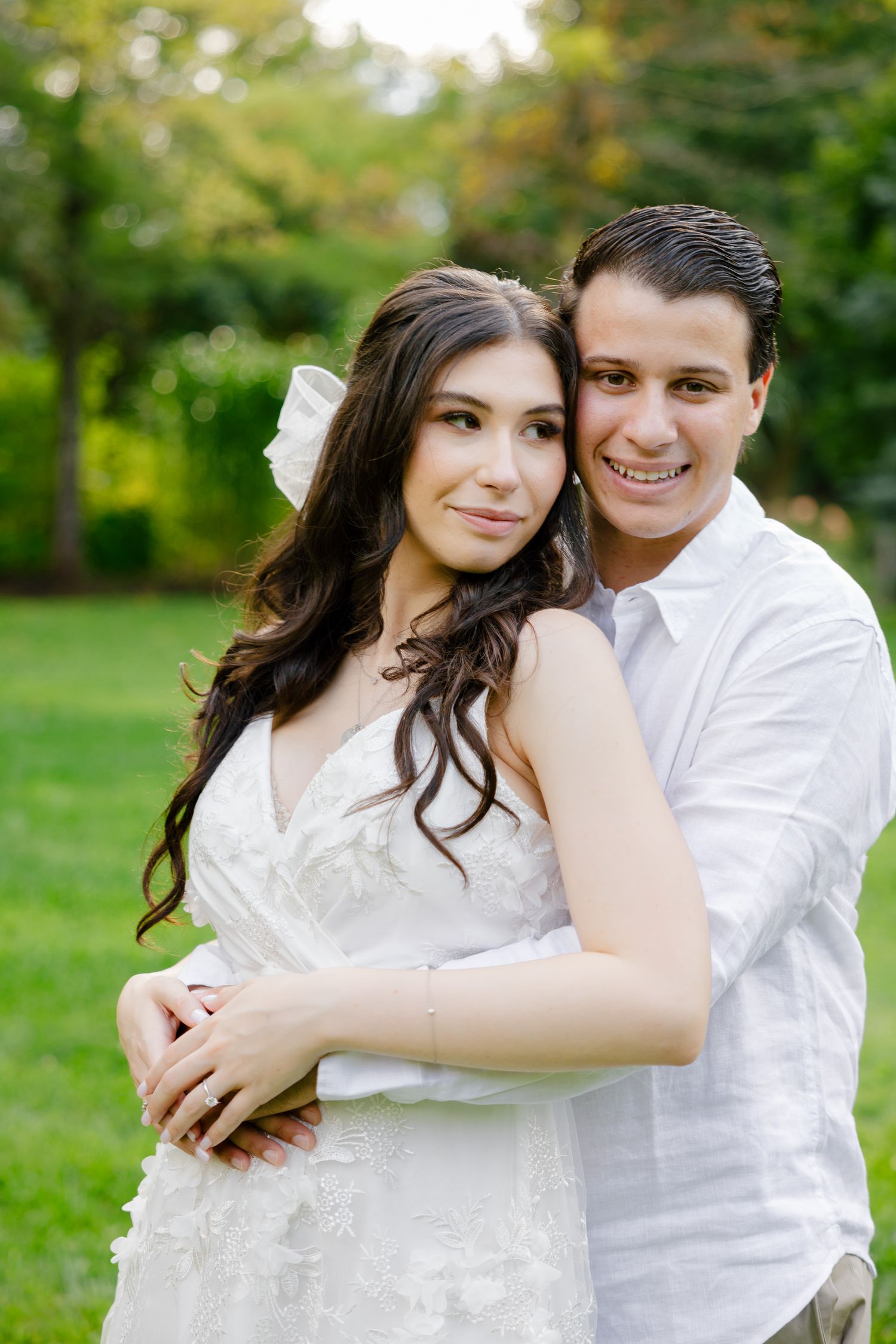 Bright outdoor engagement photo of couple in white against green garden background.