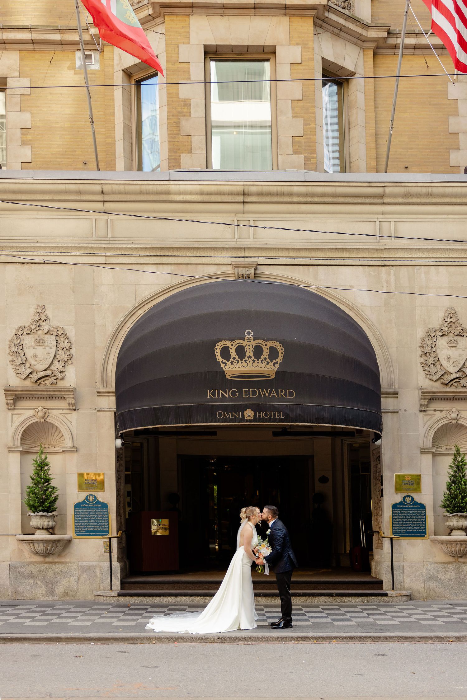Wedding photos taken outside the Kings Guard Hotel entrance with classical stone architecture and American flags.