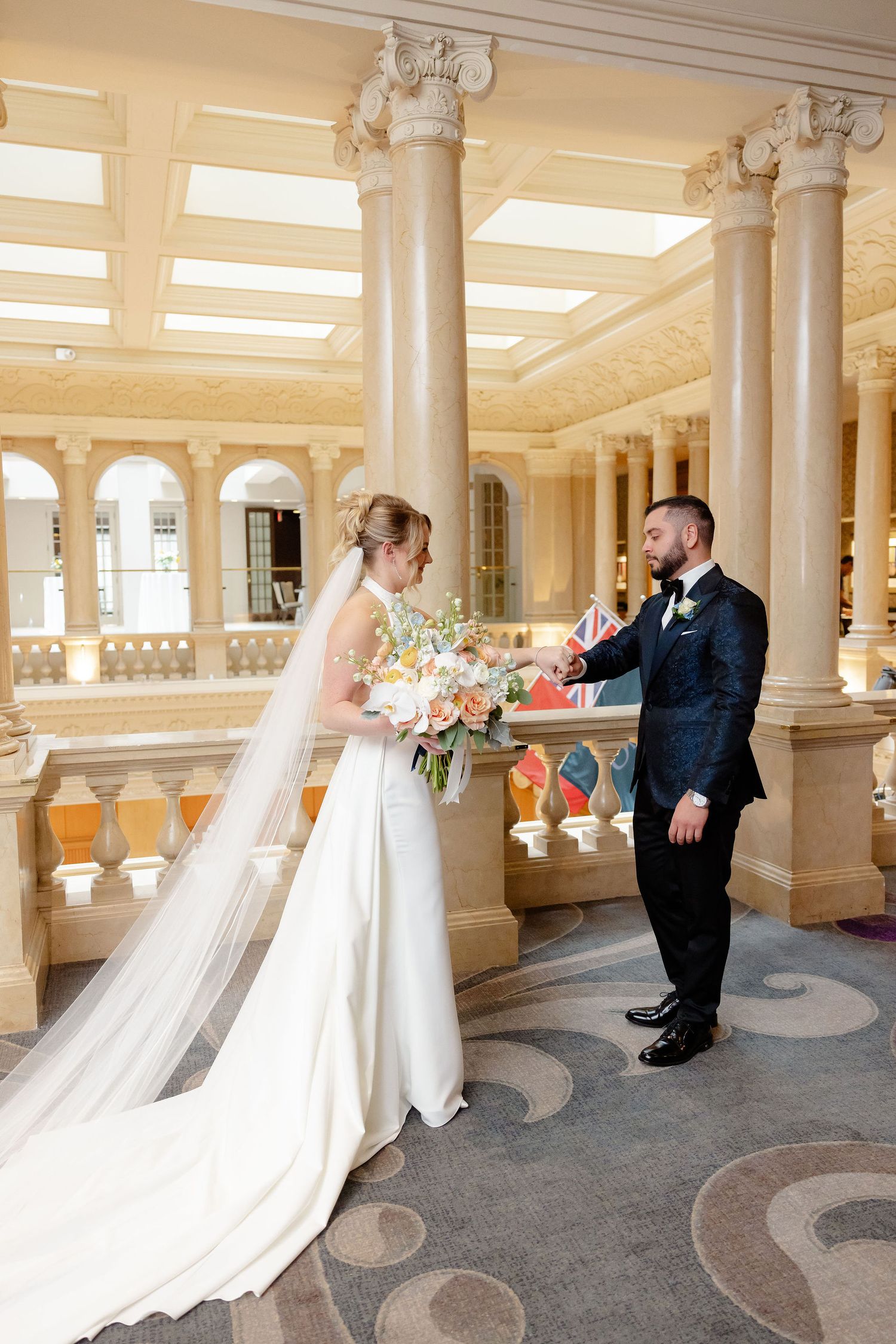 Wedding first look photos in grand columned hall with peach and blue floral bouquet.