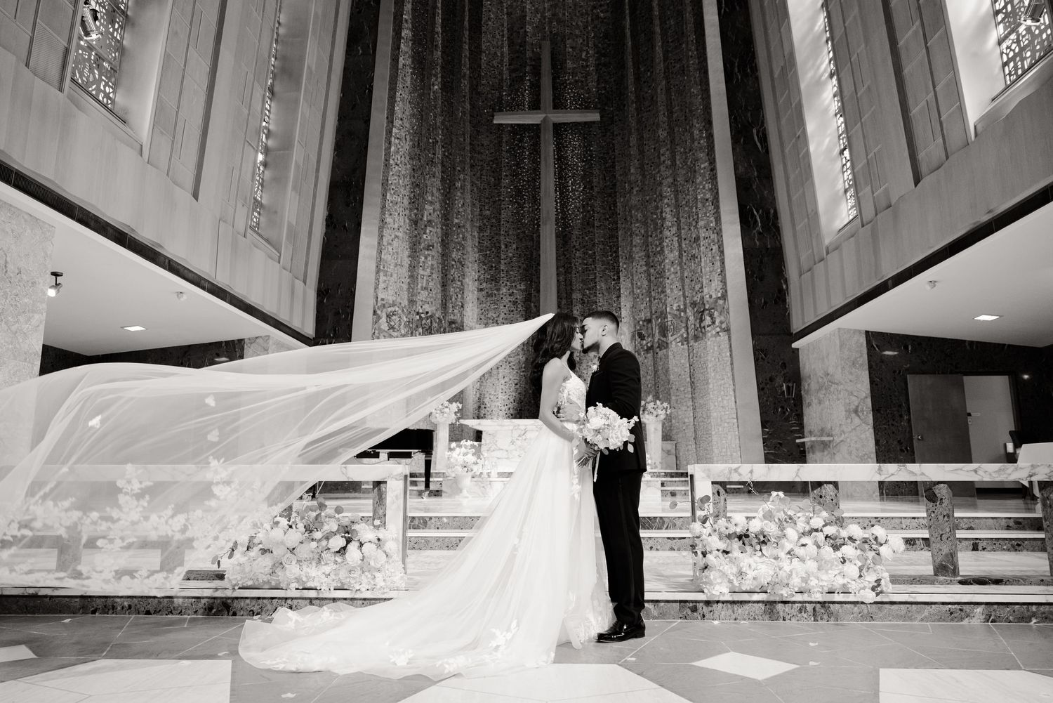 Black and white church wedding portrait with flowing veil and dramatic lighting.