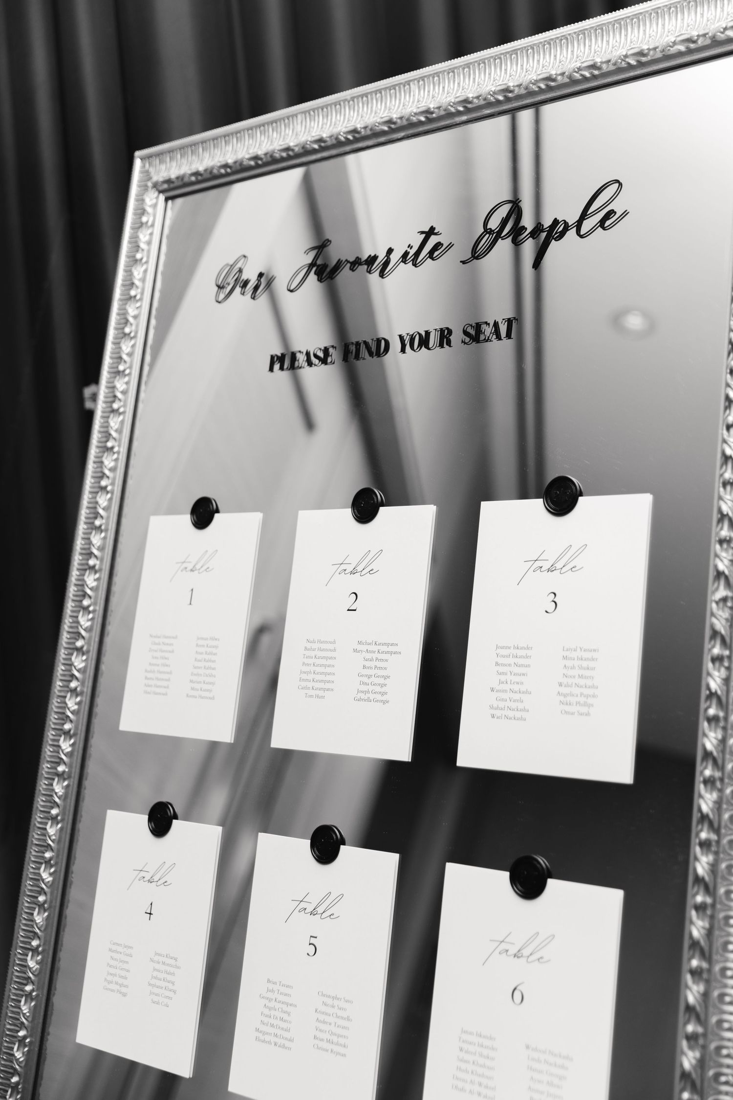 Elegant mirrored seating chart display with white cards arranged numerically in an ornate silver frame.