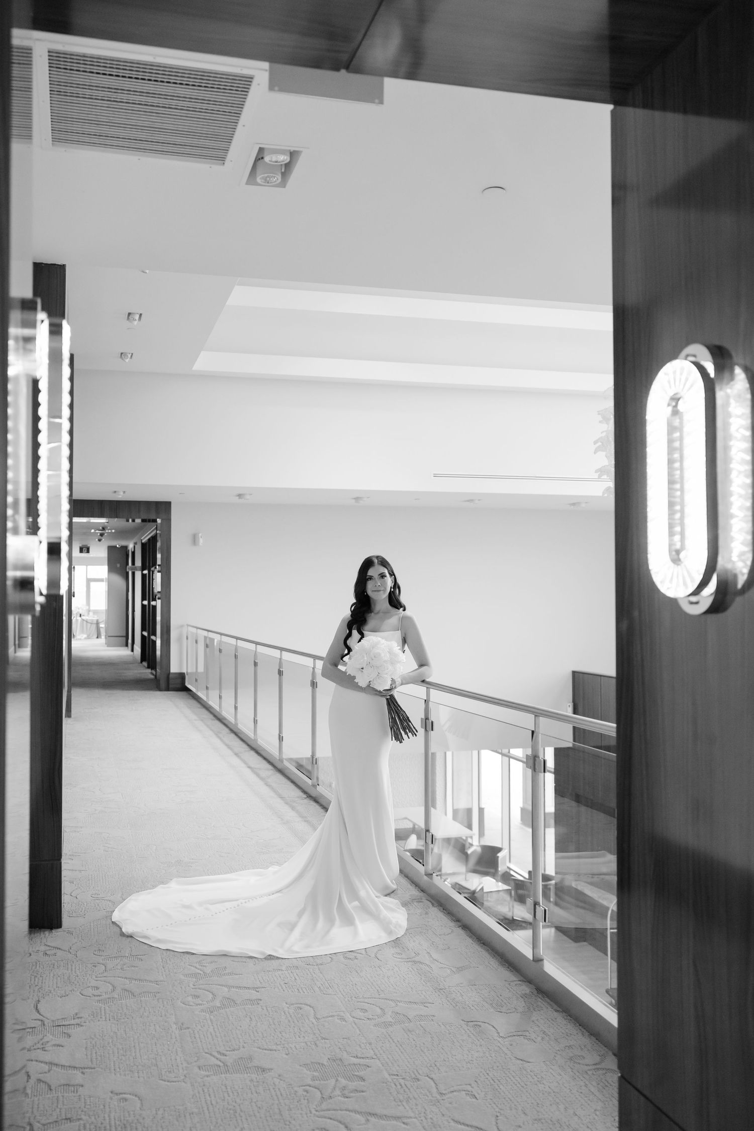 Black and white portrait of bride holding bouquet in minimalist modern hallway.
