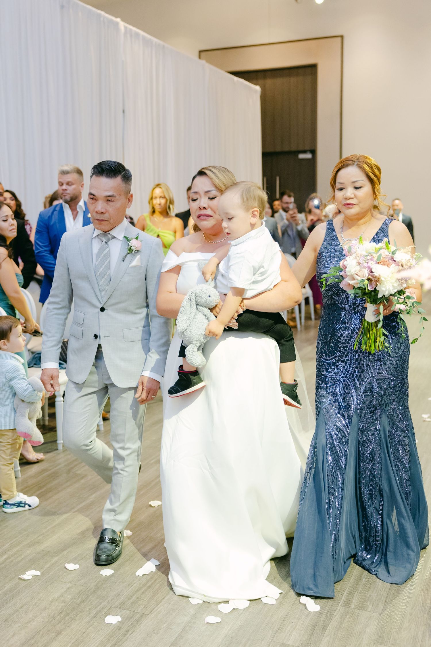 Wedding party walks down aisle after ceremony with small child and wedding flowers.