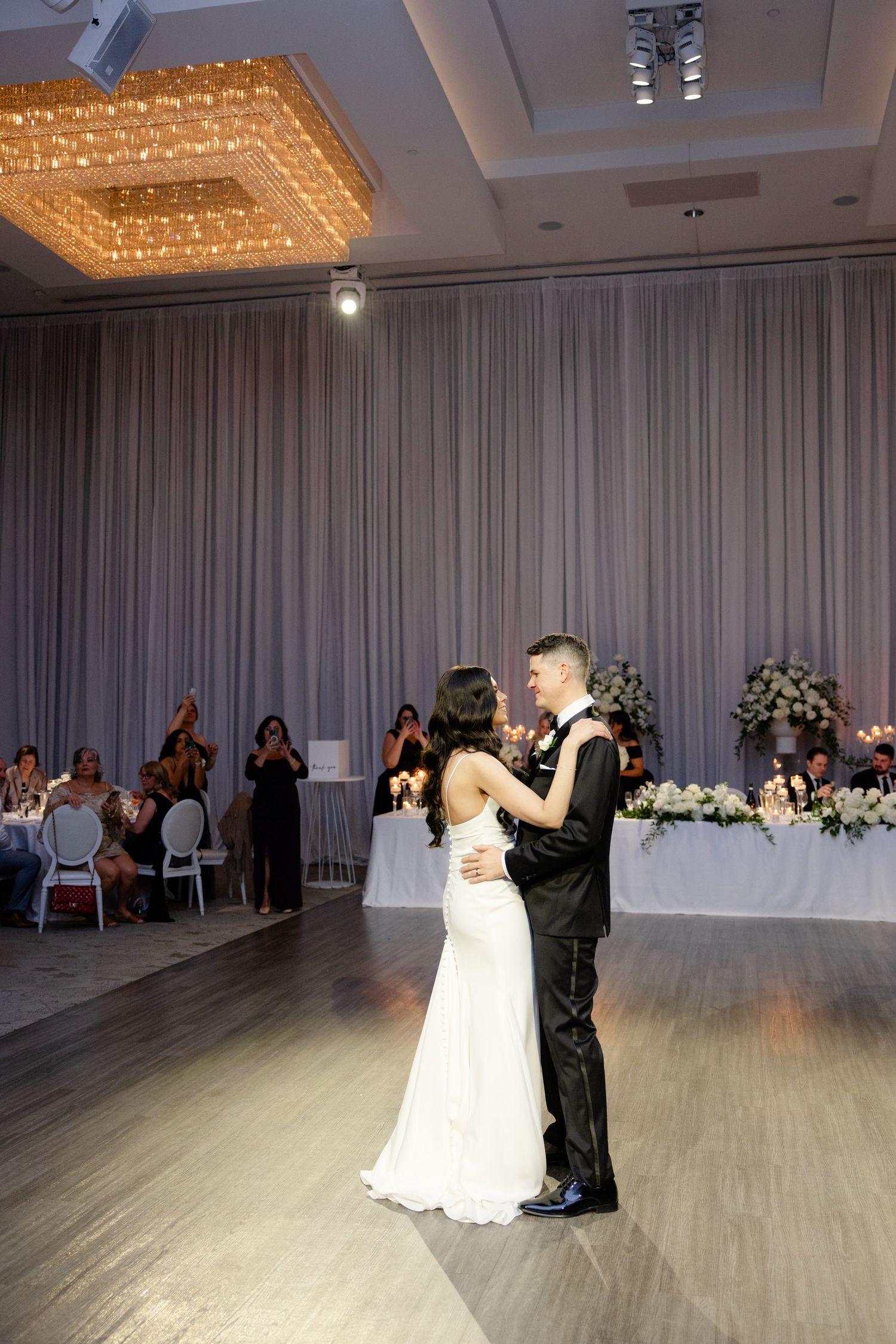 Wedding couple shares intimate first dance under elegant chandelier in reception venue.