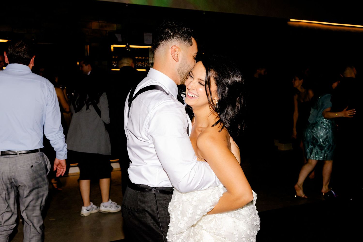 Couple embracing during their wedding reception dance on darkened dance floor.