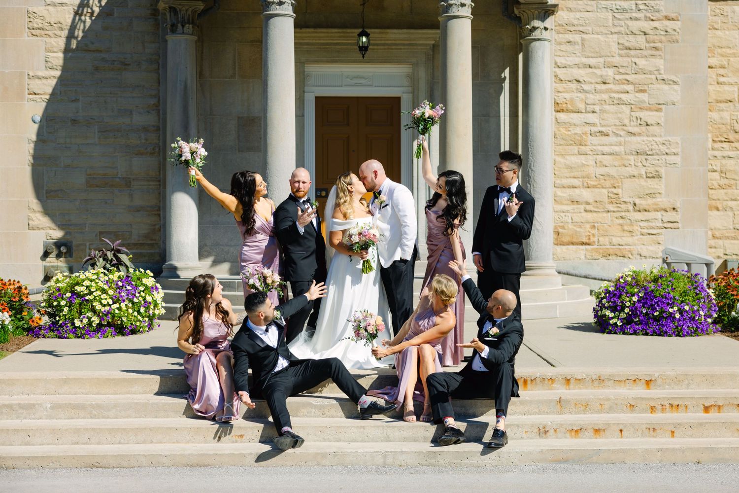 Fun wedding party photo with group striking playful poses on building steps.