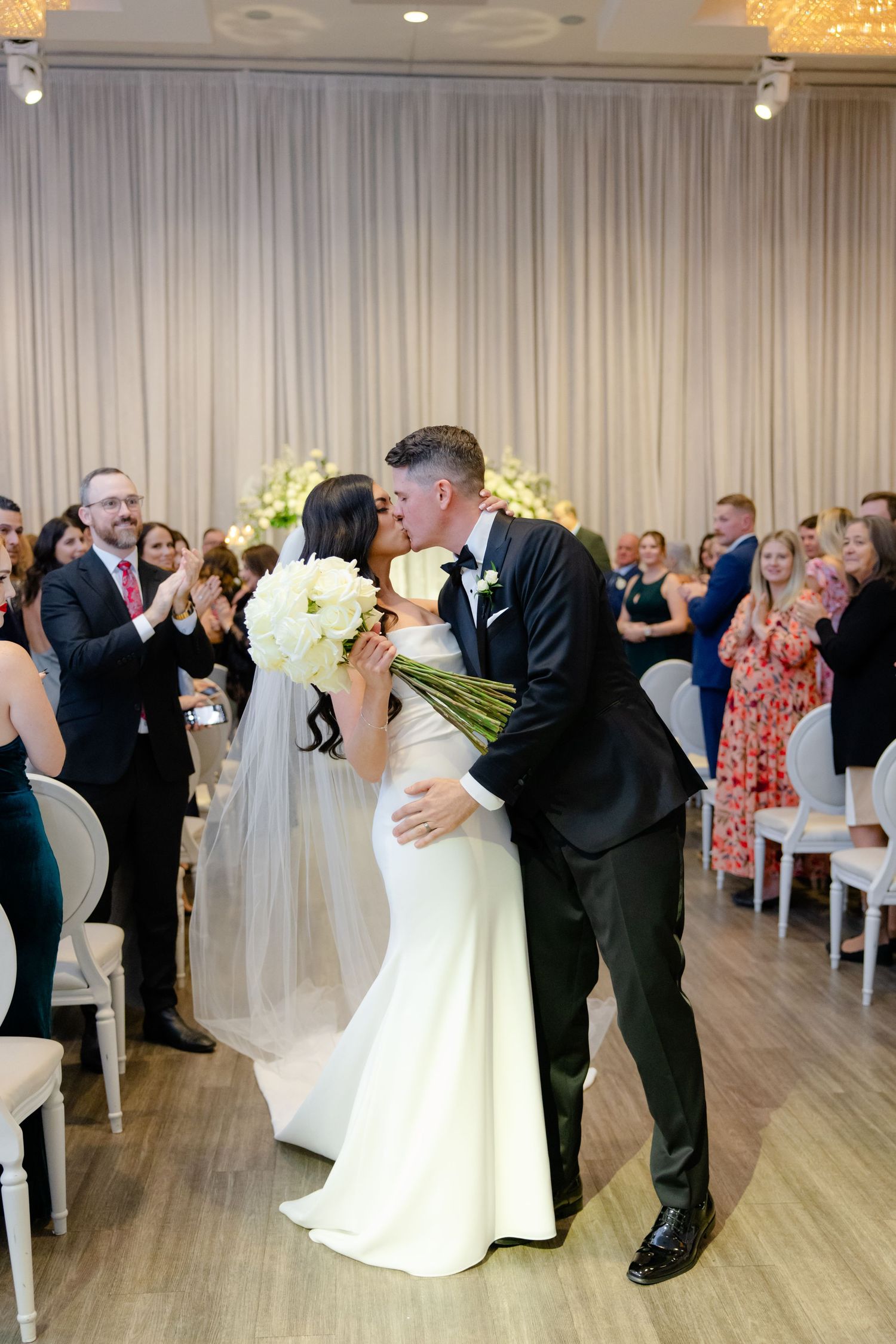 A wedding ceremony kiss in an elegant ballroom filled with guests.