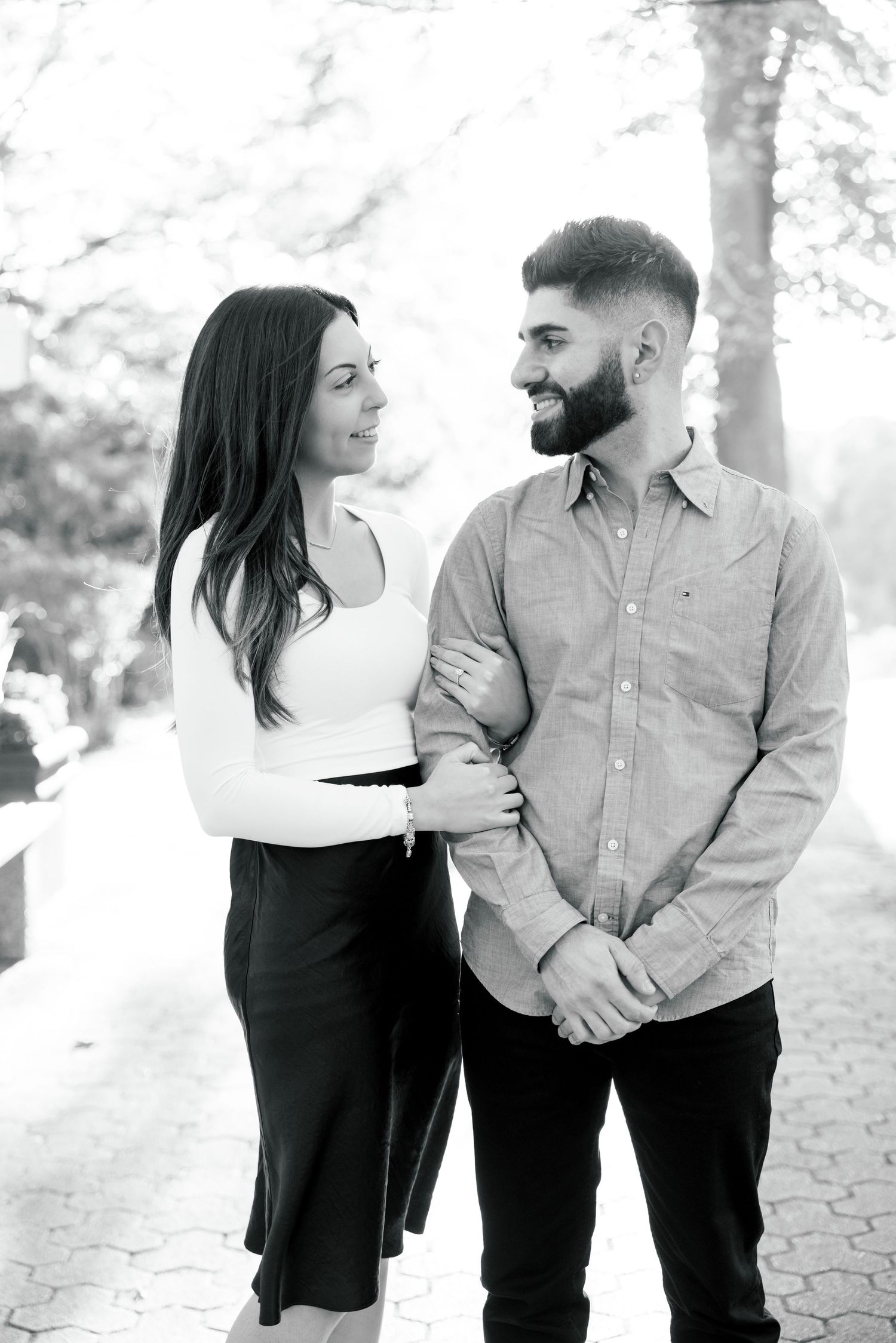 A romantic black and white portrait of a couple in casual attire gazing at each other in an outdoor setting.