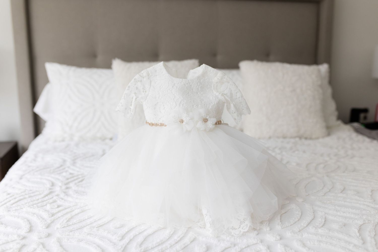 White baptism dress laid out on white textured bedding.