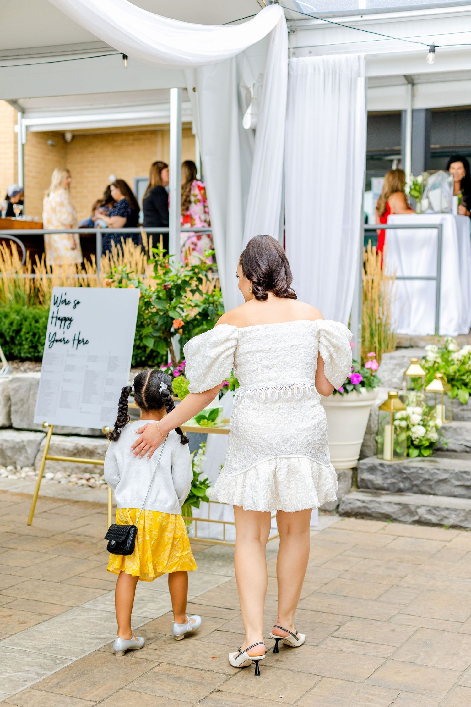 Adult and child walking together at an outdoor event with white tent decor.