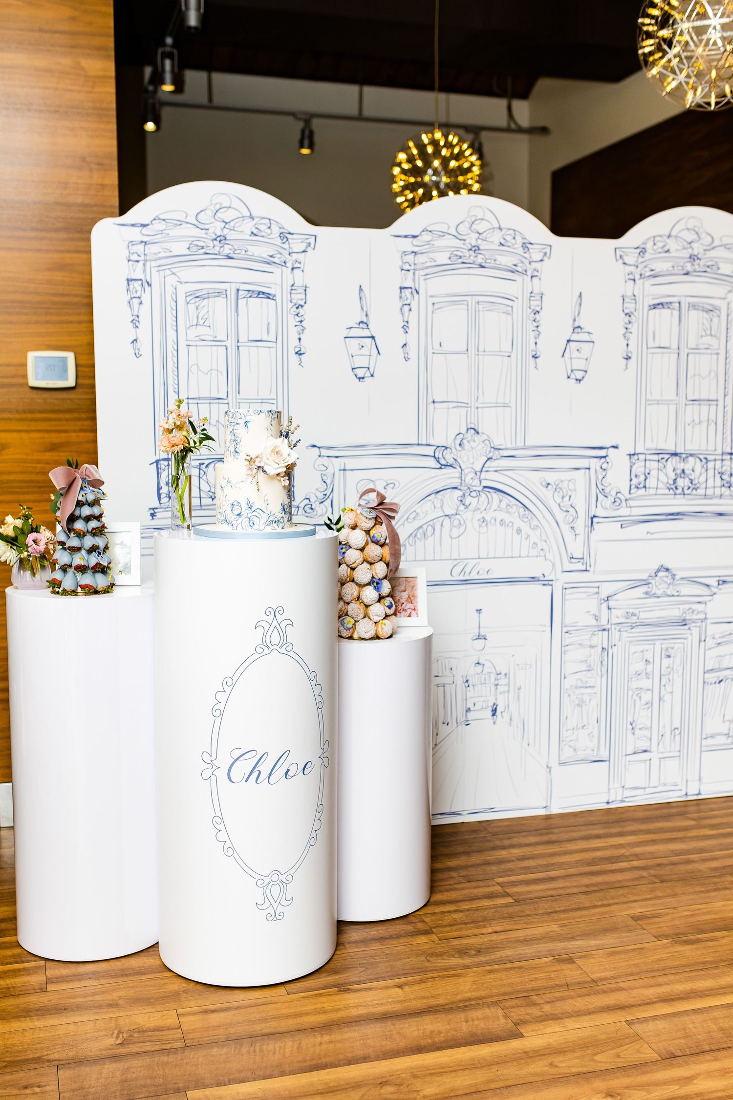 White decorative pedestals with floral arrangements against a blue sketched architectural backdrop.