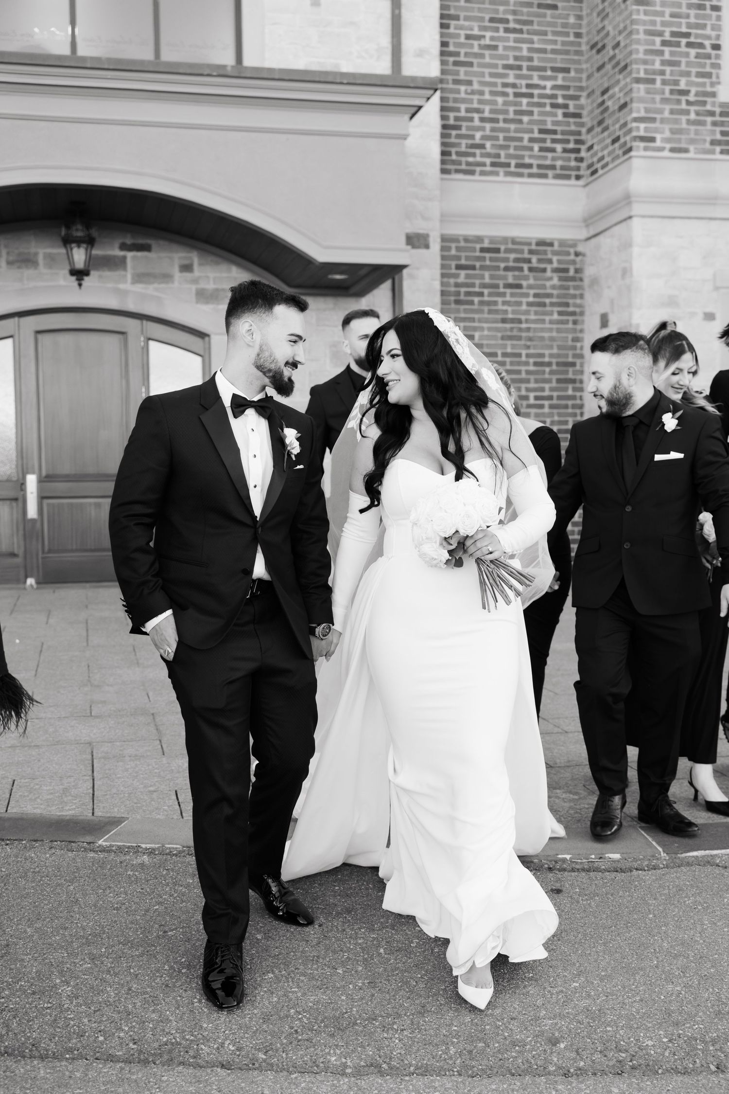 Black and white portrait of couple in wedding attire sharing a joyful moment outside.