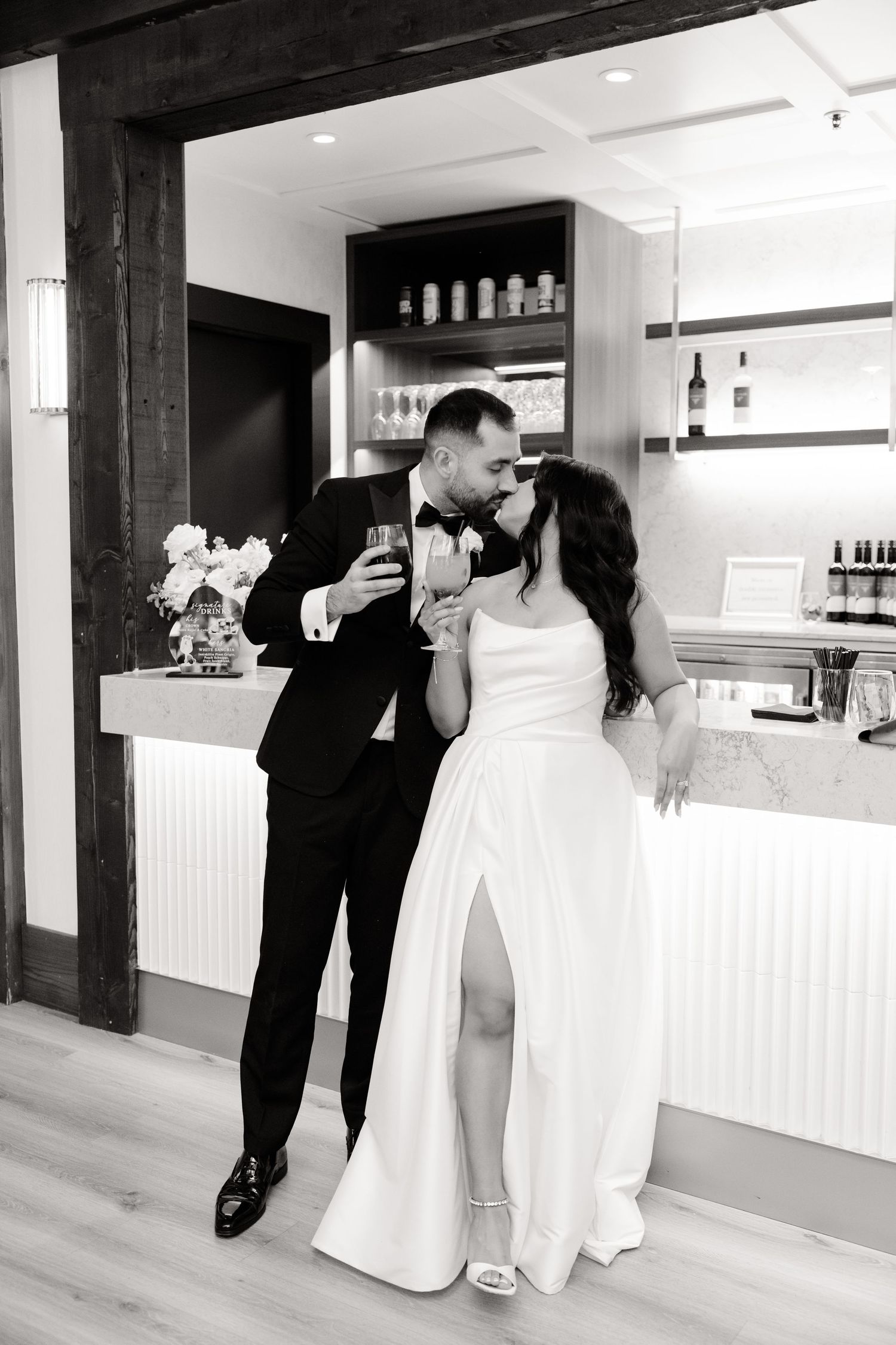 Black and white photo of couple laughing while toasting at an elegant wedding reception bar.