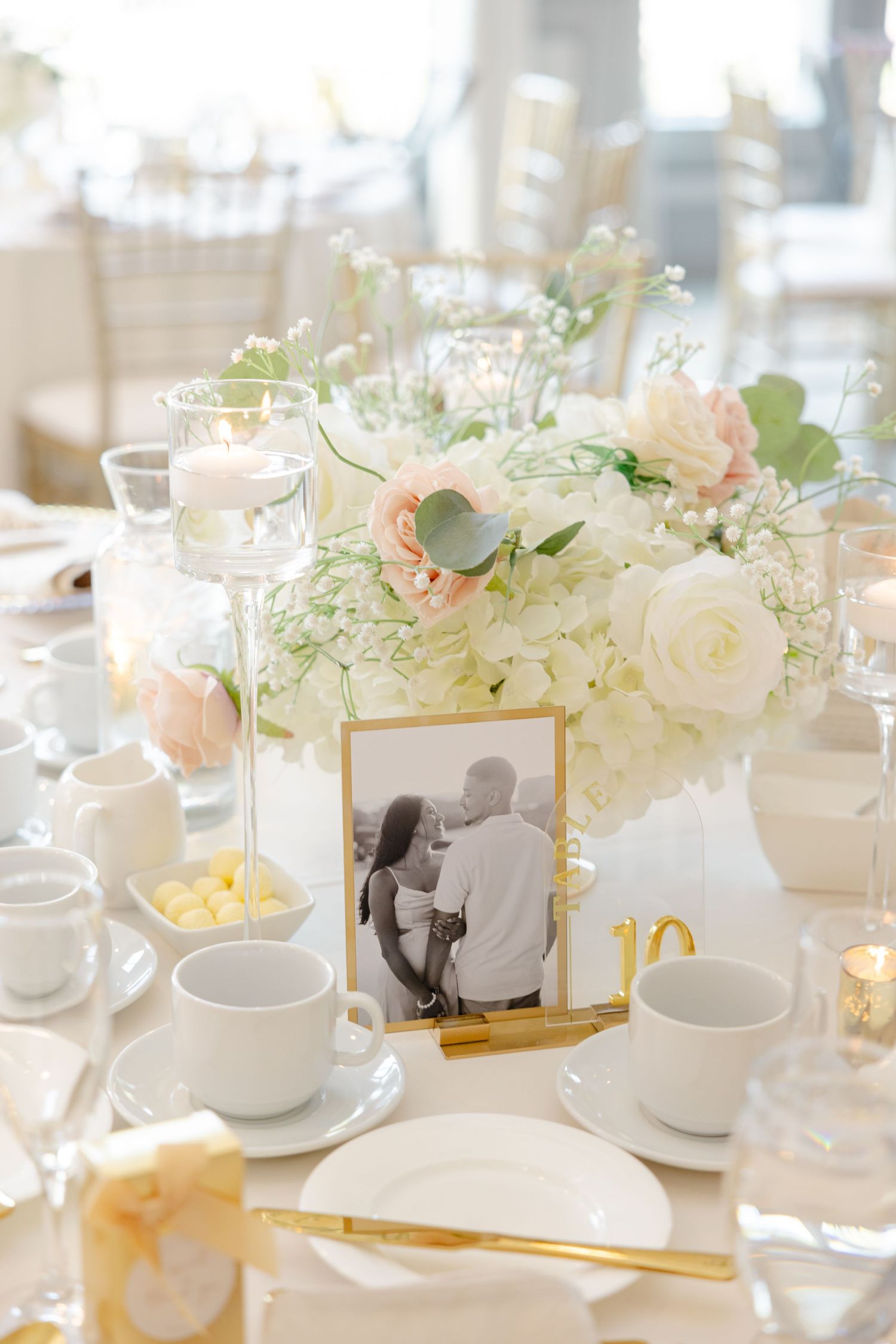 Romantic table centerpiece with white roses, candles, and framed photograph in gold frame.