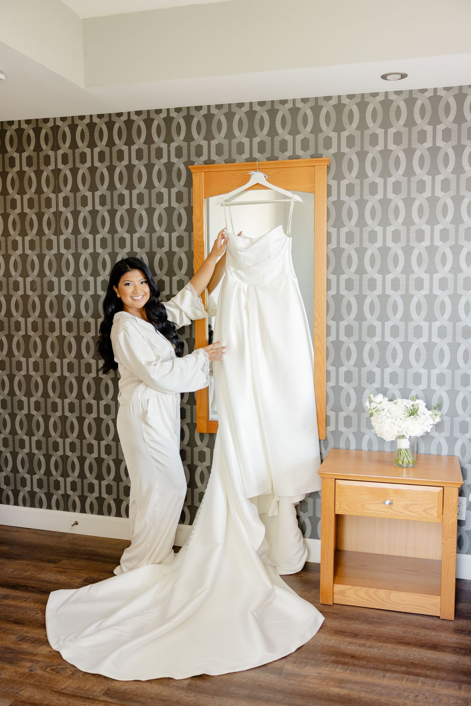 Wedding dress being arranged against modern geometric wallpaper in preparation room.