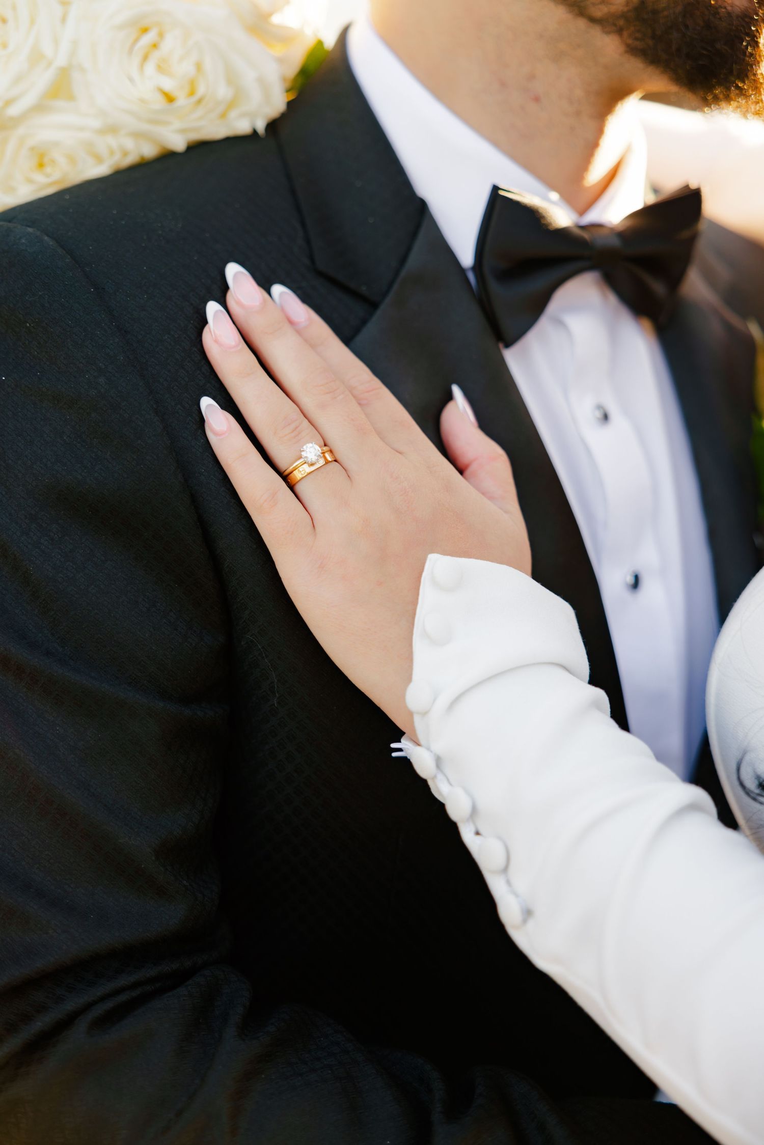 Close-up of bride's hand with wedding ring resting on groom's black tuxedo lapel.