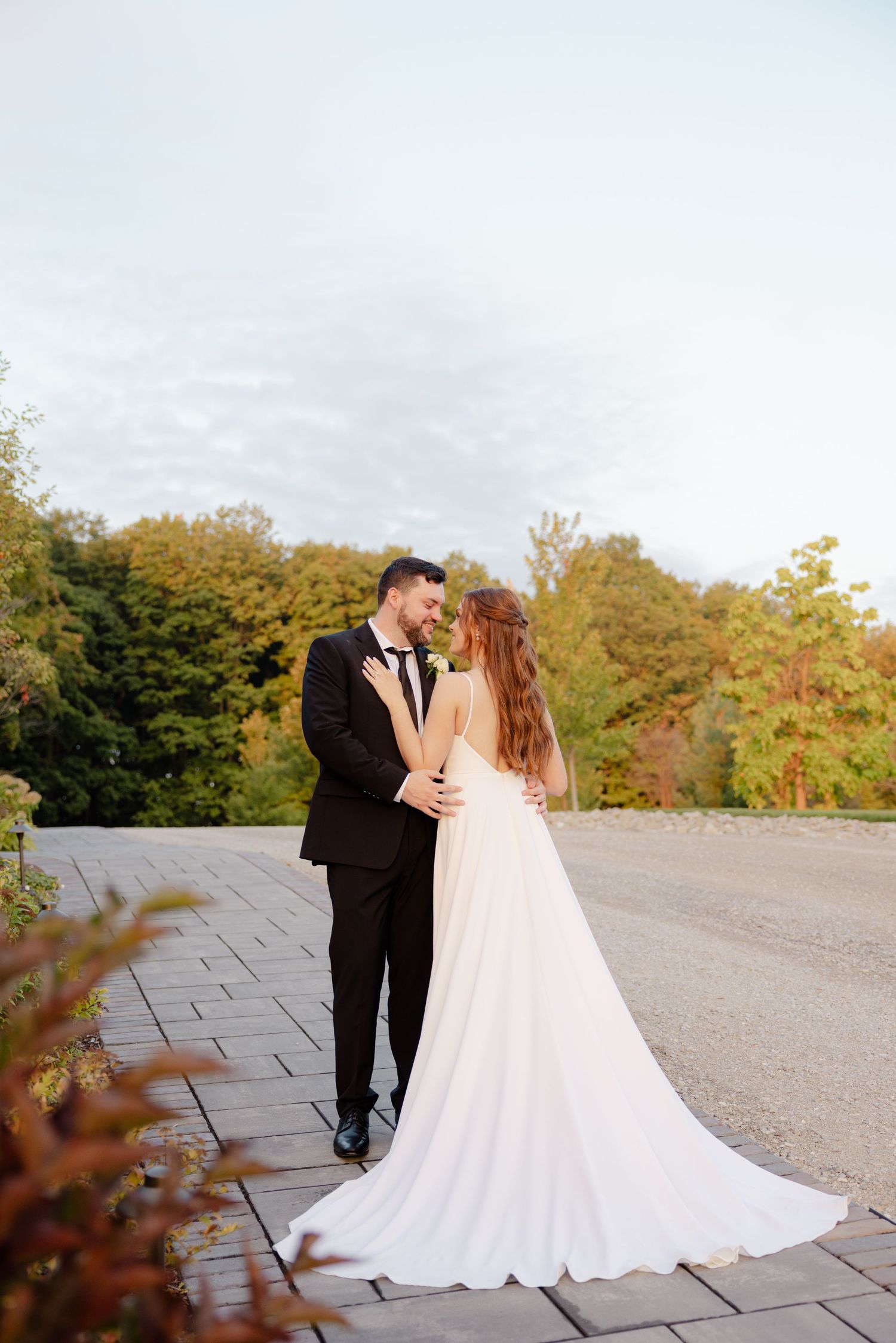 A romantic wedding couple embraces on a stone pathway surrounded by autumn foliage on their special day.