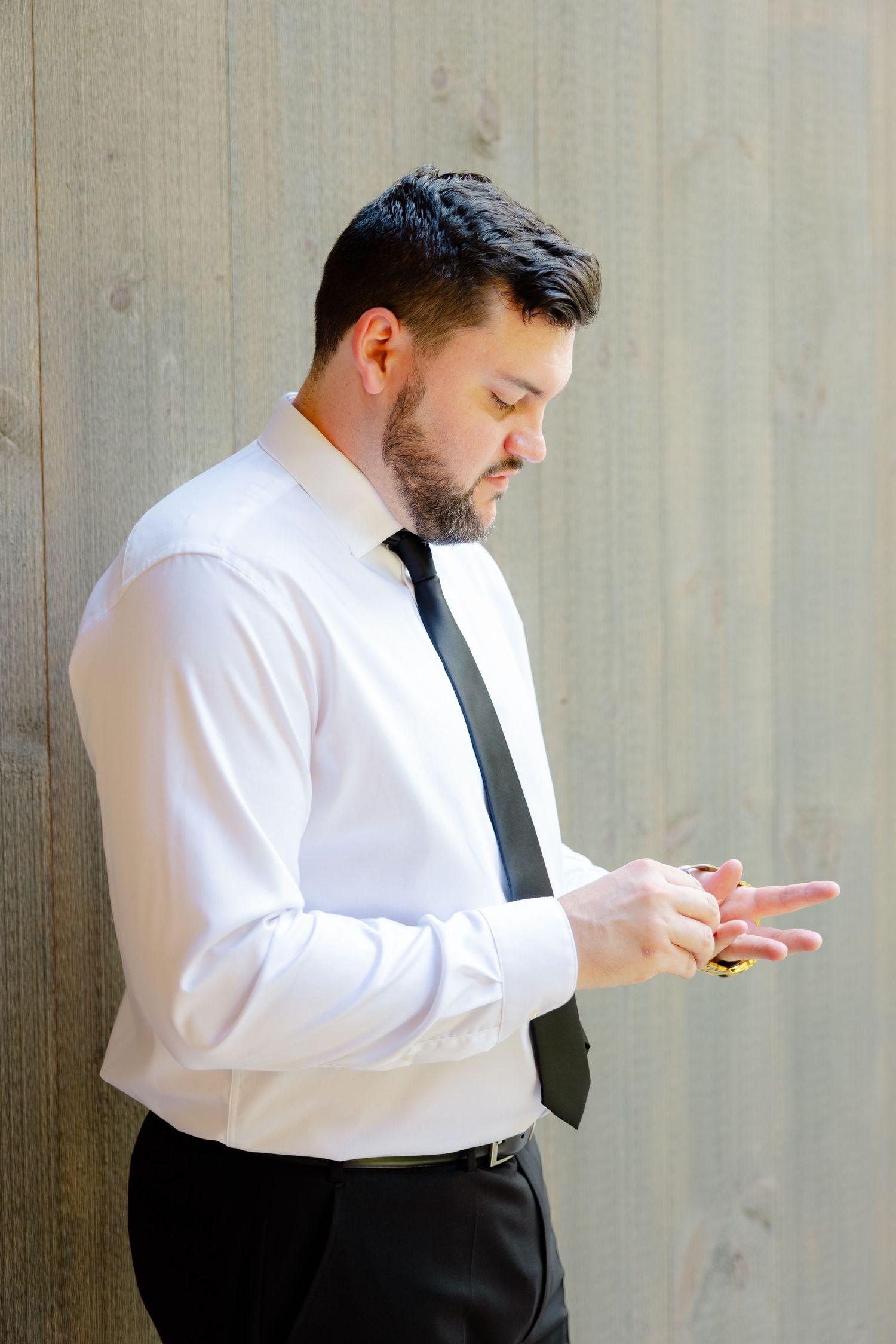 Person in formal white shirt and tie looking down at phone against wooden wall.