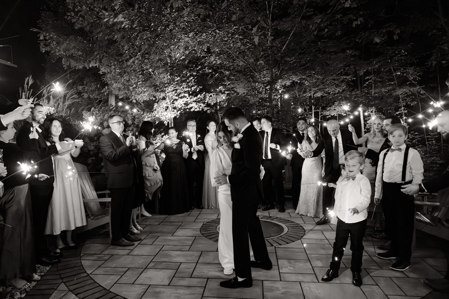 A black and white photo captures a couple's wedding dance surrounded by guests with sparklers.
