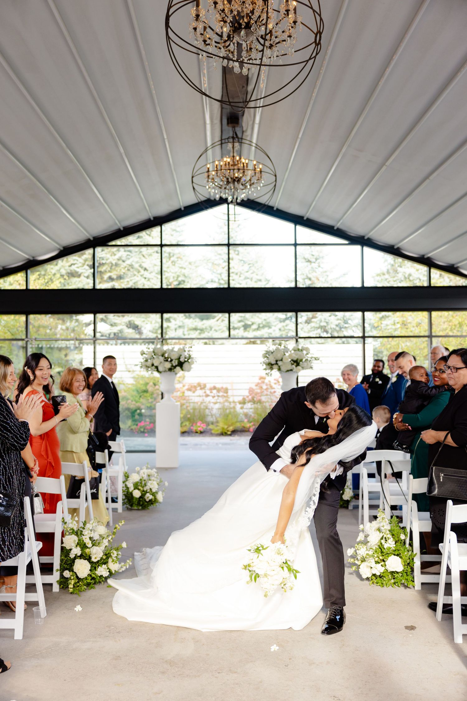 A romantic dip kiss during wedding ceremony while guests applaud in an elegant indoor venue.