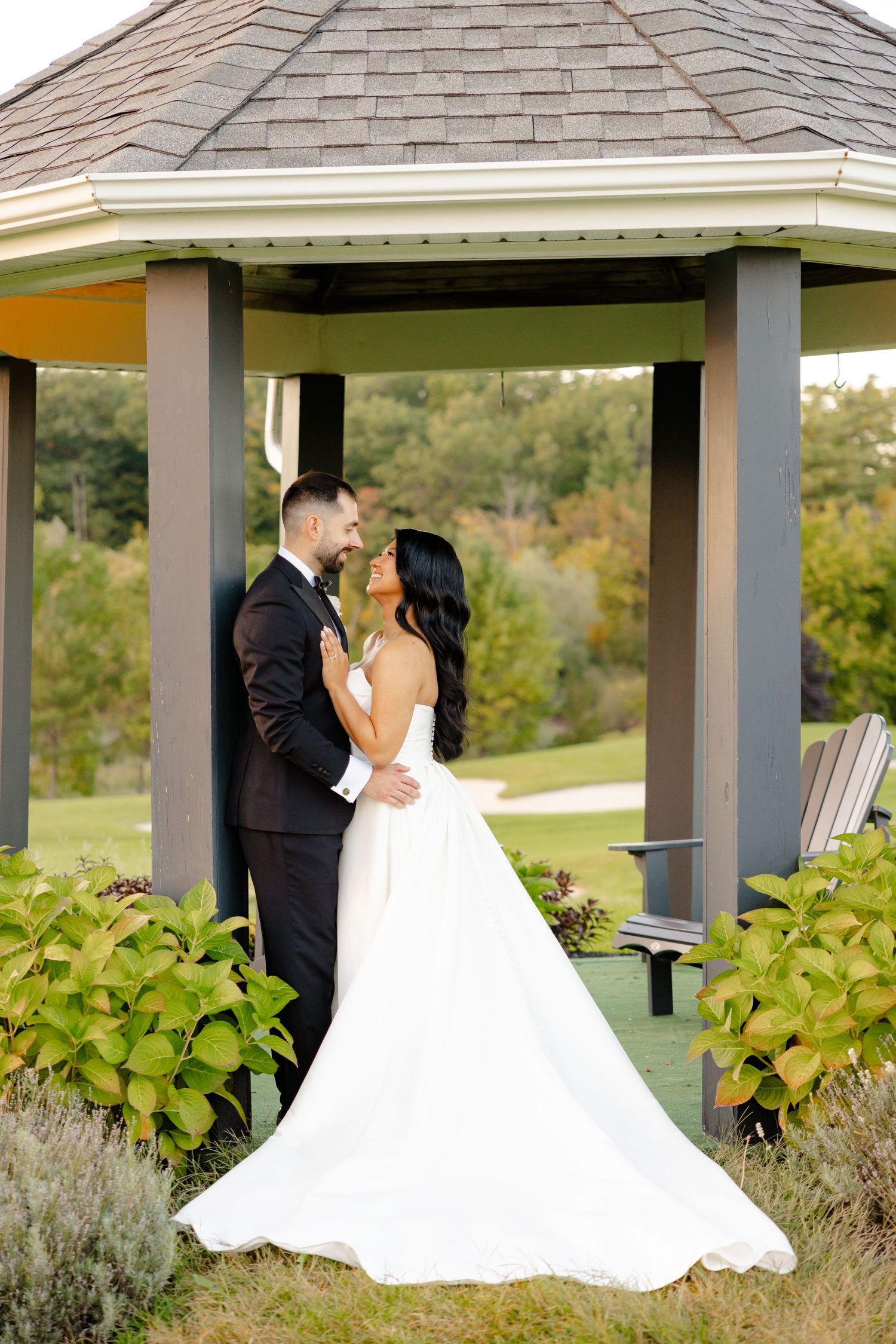 A wedding couple embraces under a tiered roof gazebo surrounded by ornamental plants and lavender.