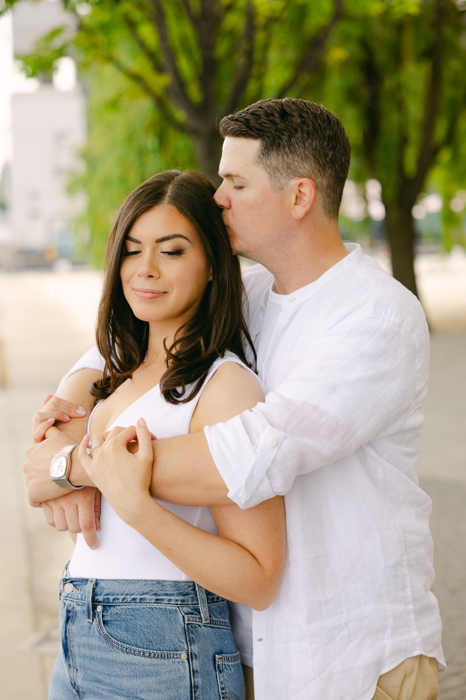 An intimate portrait of a couple embracing outdoors with lush greenery in the background.