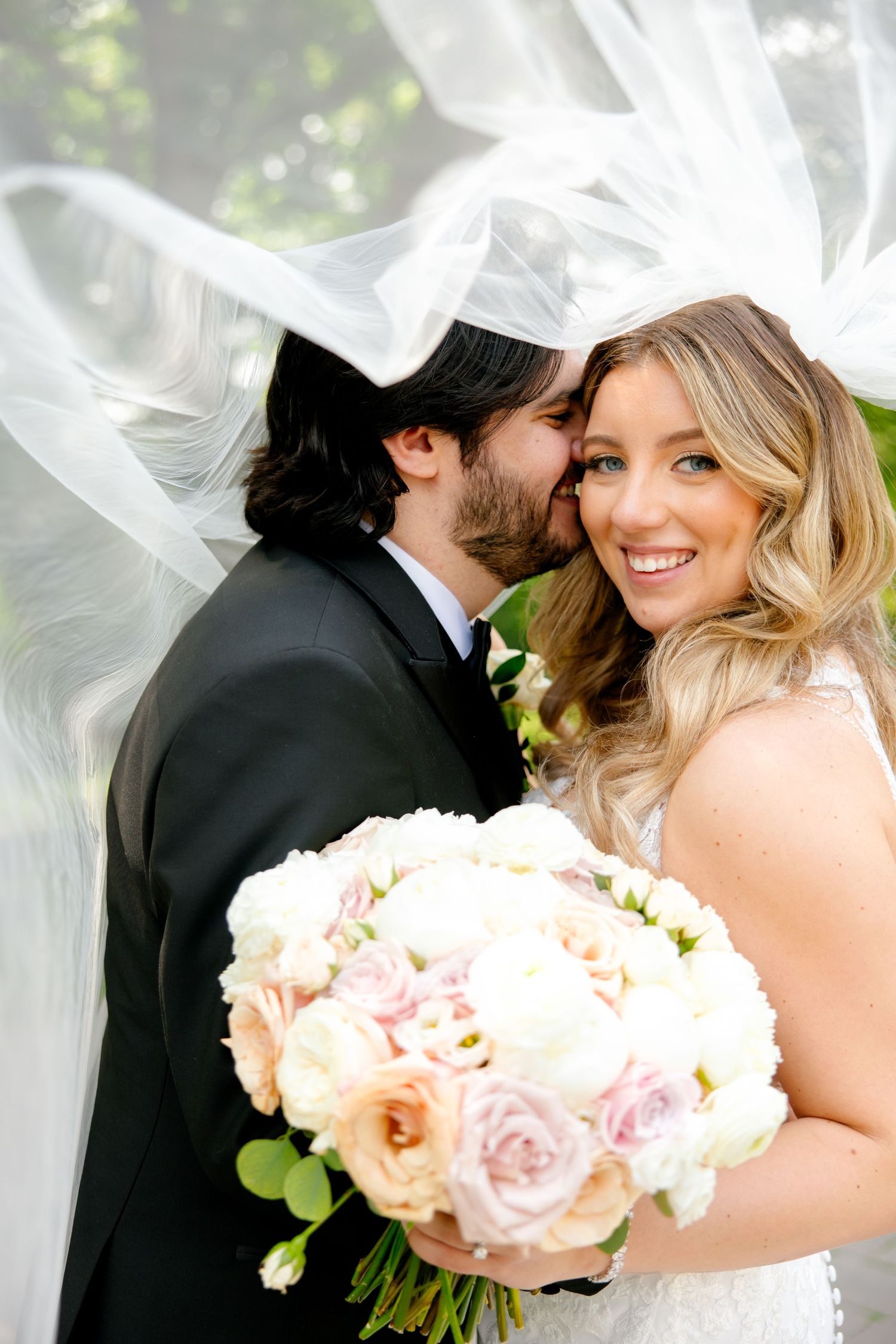 An intimate garden wedding moment with flowing veil and delicate peach and pink bouquet.