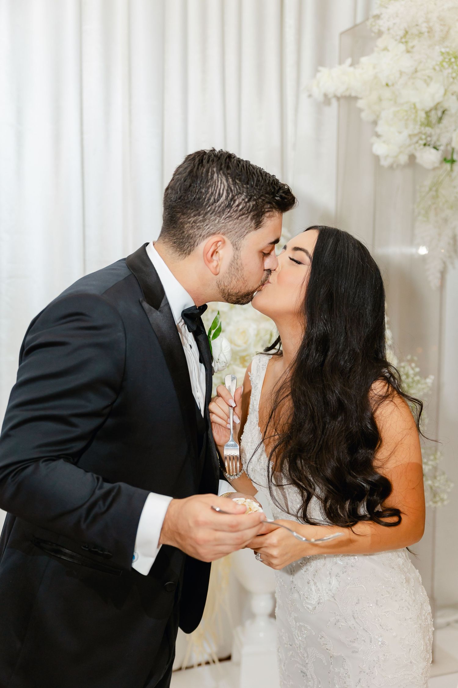 Wedding couple sharing a tender kiss with white floral decor in the background at a luxurious venue.