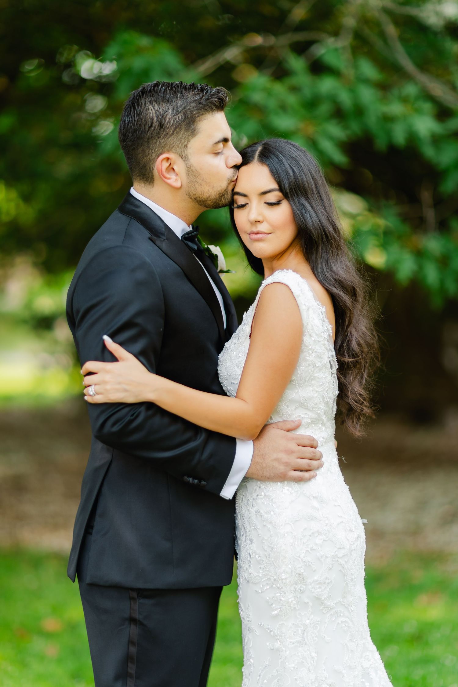 Tender moment between newlyweds in formal attire captured in a lush garden setting.