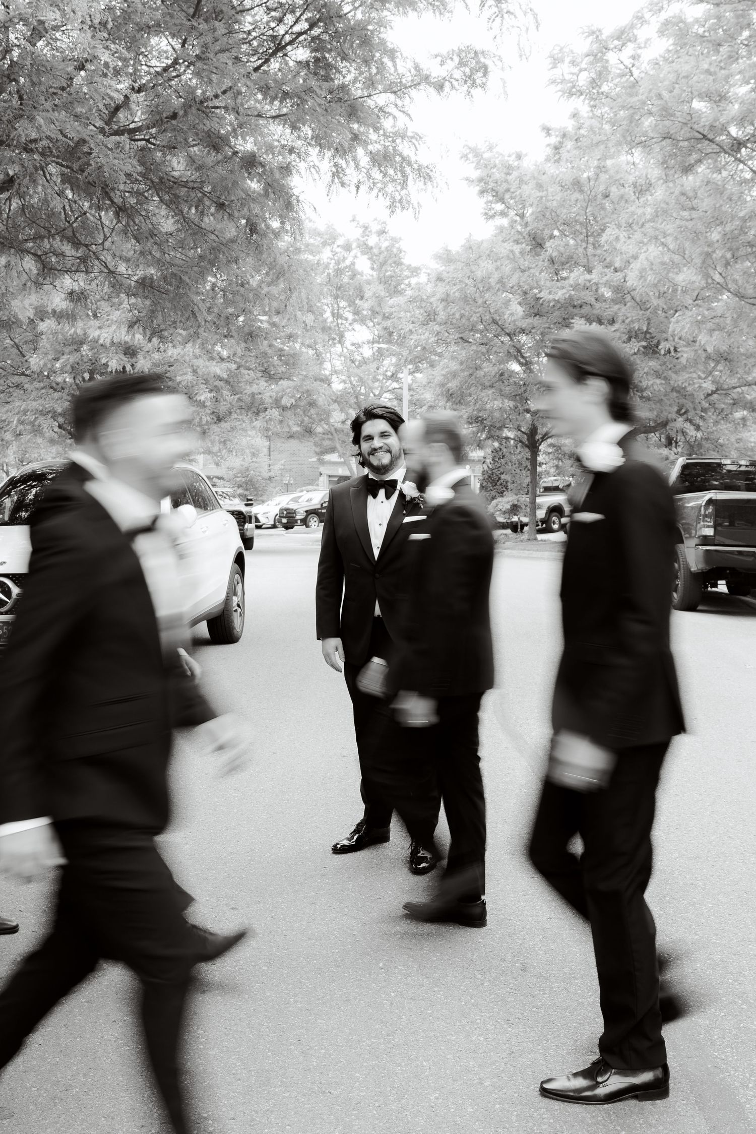 Artistic black and white photo of groomsmen in motion around central figure in tuxedo.