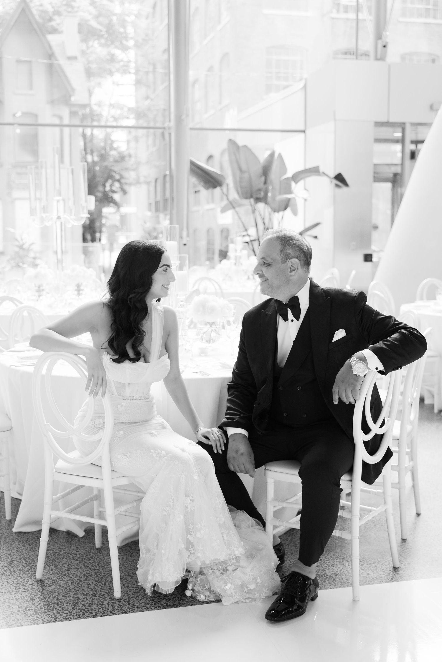 Black and white photograph of newlyweds sitting together in modern reception venue.