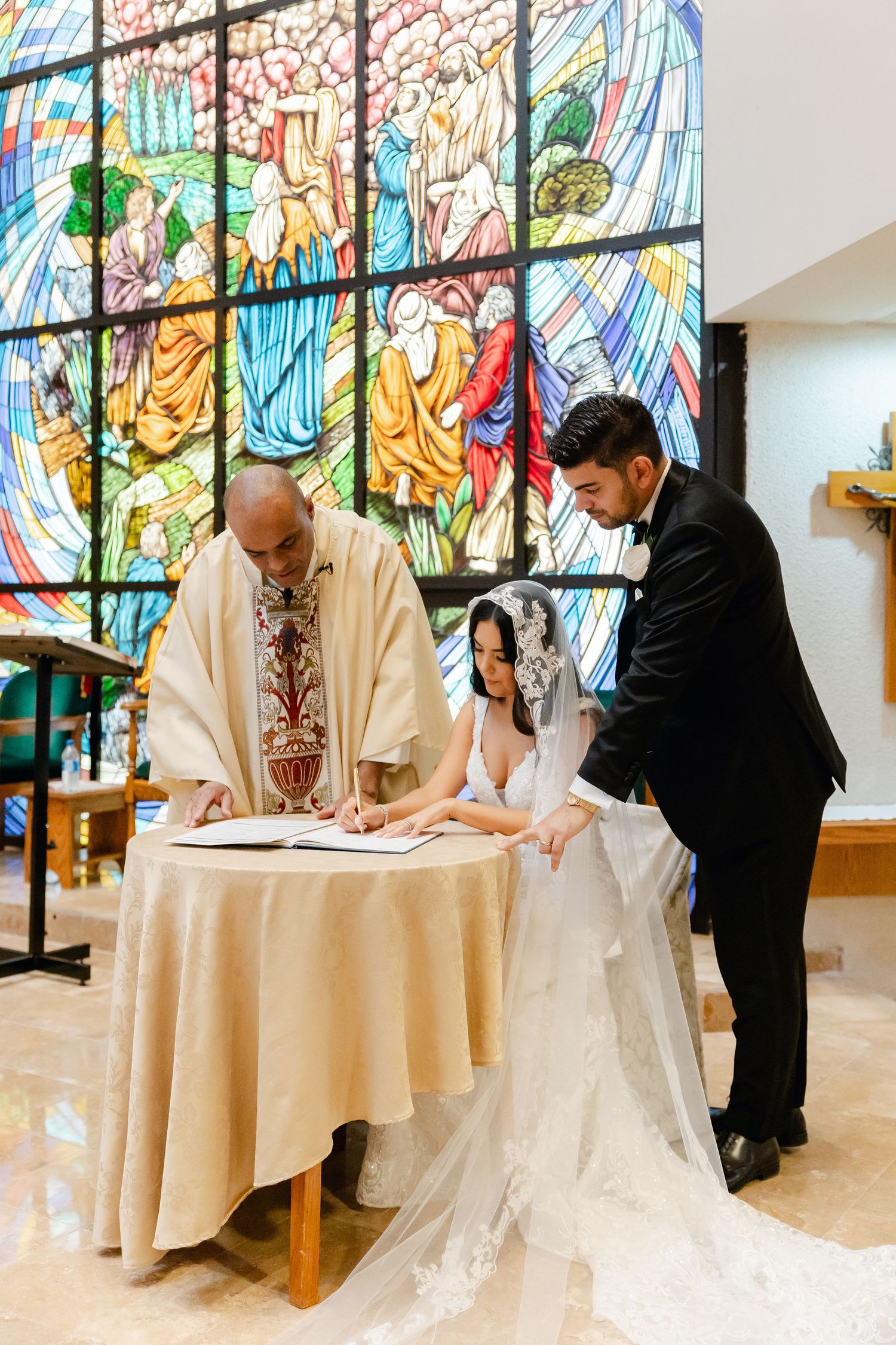 Wedding ceremony with priest officiating at altar under colorful stained glass window.