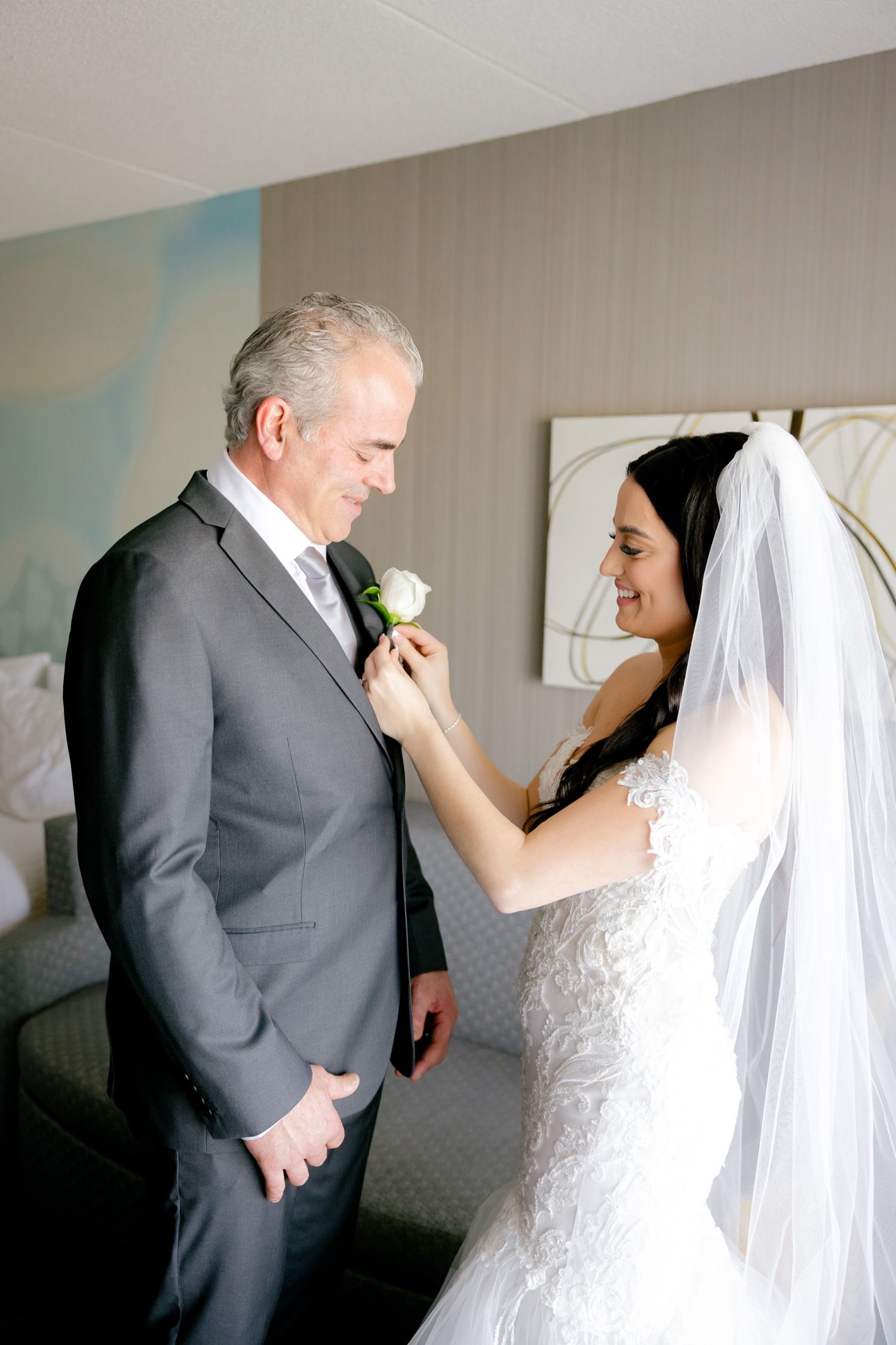 Sweet moment of bride adjusting boutonniere on suit lapel during wedding preparations.