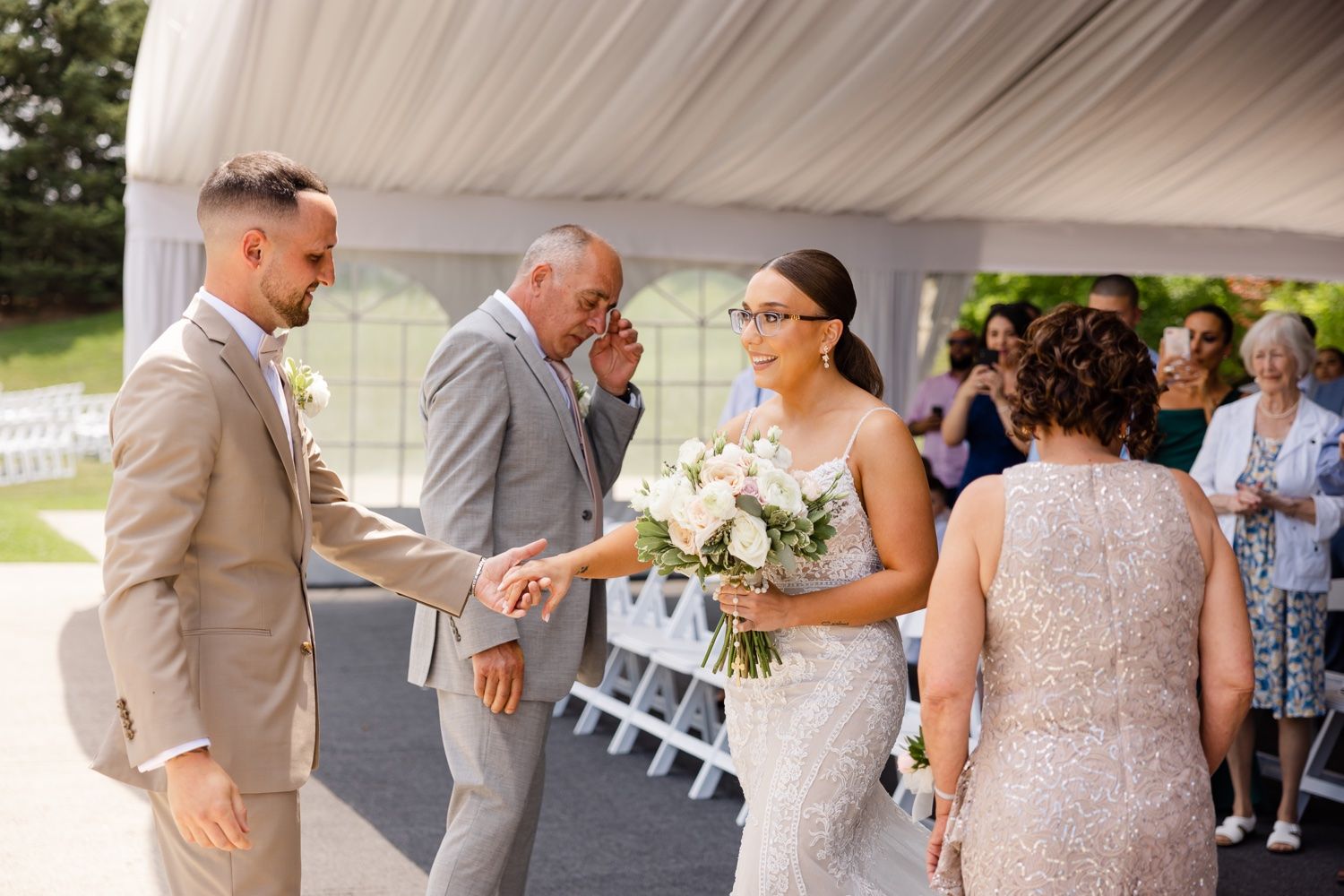 Wedding ceremony guests gather under an elegant white tent canopy for a celebration.