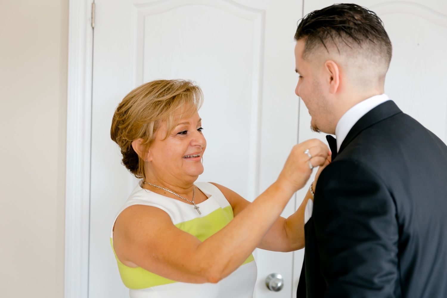 Woman in yellow dress helps adjust groom's formal attire before ceremony.