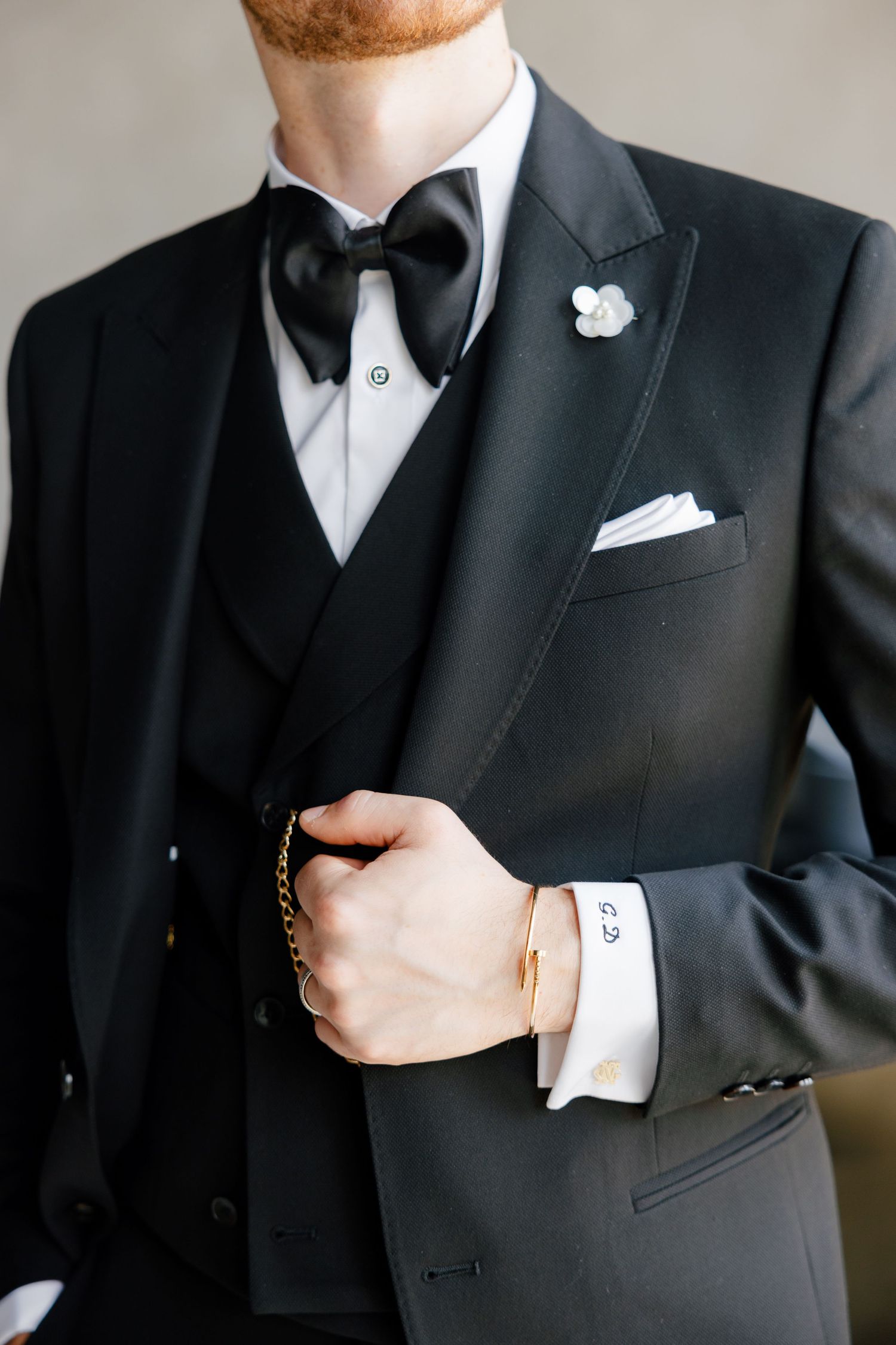 Close-up detail of a black tuxedo with bow tie, pocket square, and white boutonniere.