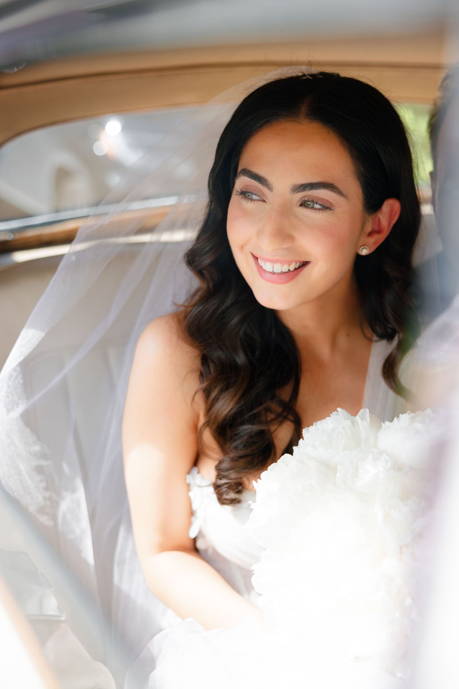 Close-up portrait of bride smiling in vintage car on wedding day.