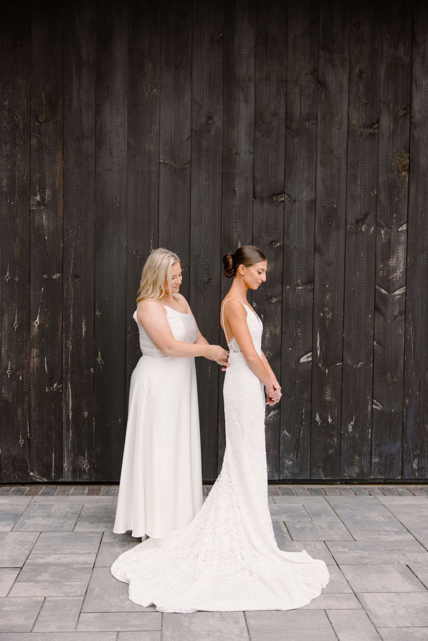 Two elegant wedding dresses shown against rustic wooden wall backdrop.