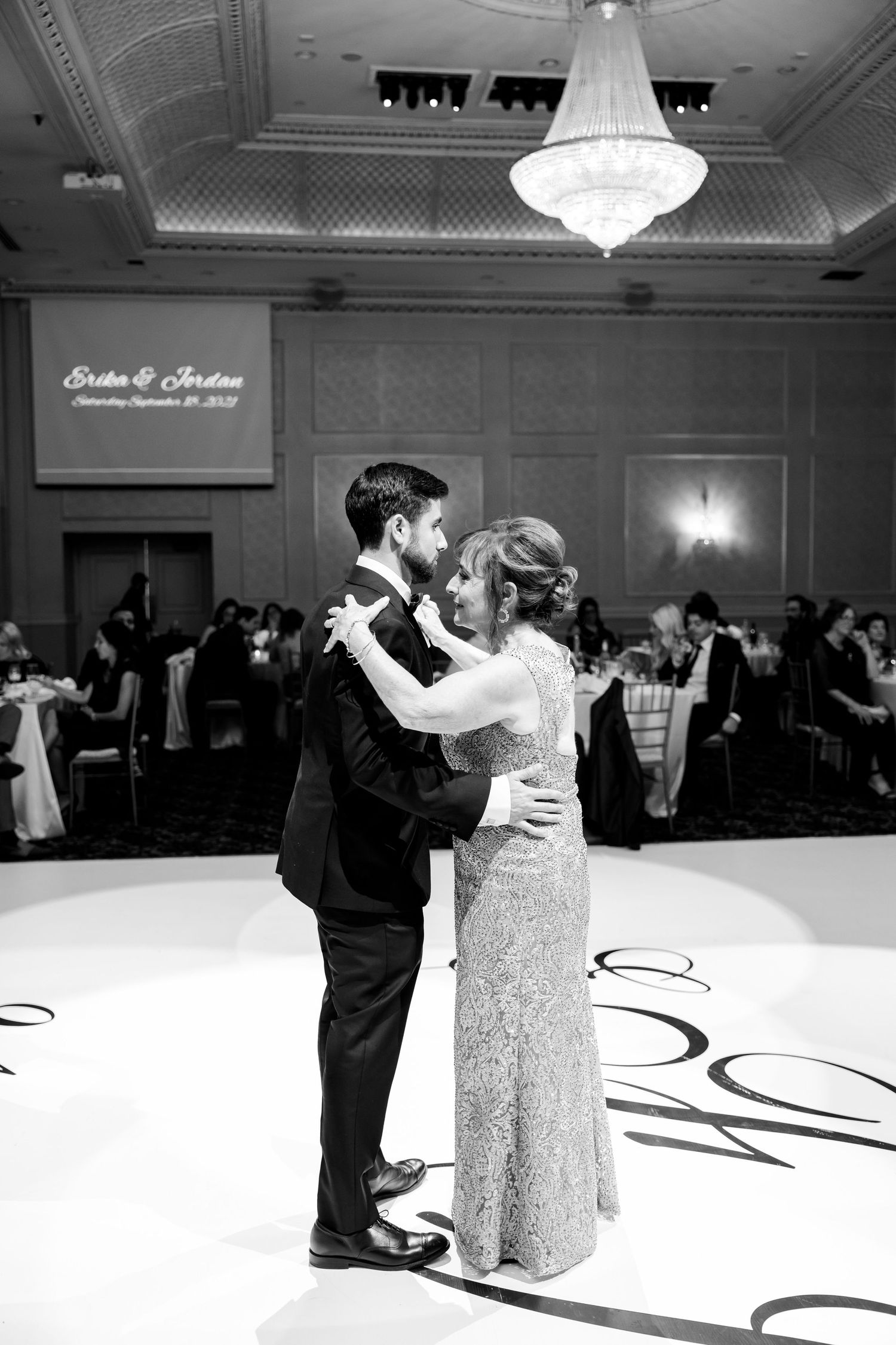 A romantic black and white photo of a first dance beneath a crystal chandelier.