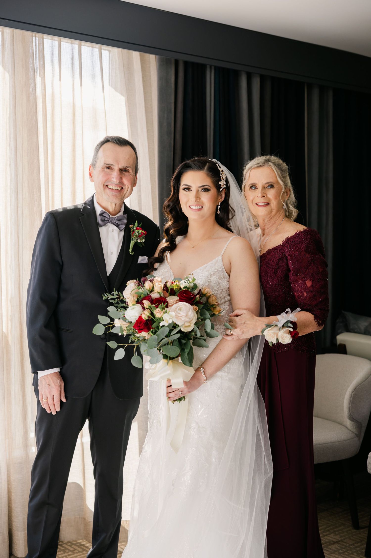 Wedding party portrait with bride in white gown flanked by two guests in formal attire.