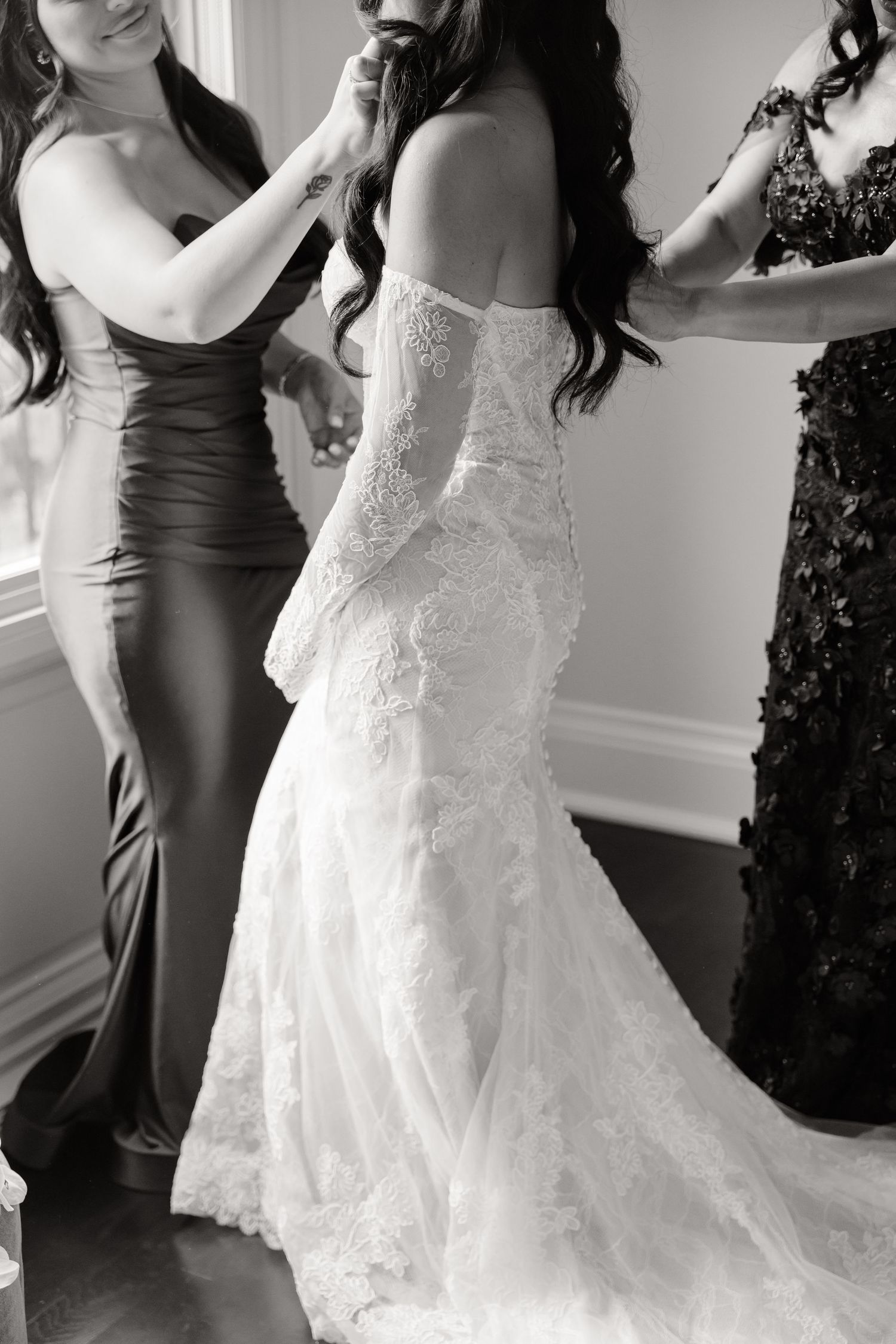 Black and white photos show wedding preparations as attendants help adjust a flowing white lace bridal gown.