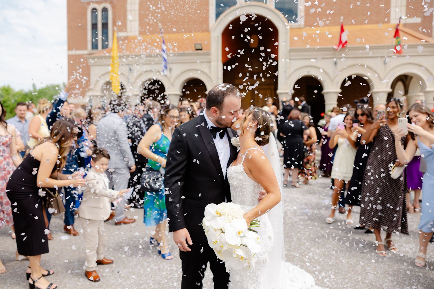Wedding couple exits church as guests shower them with white confetti during joyful celebration.