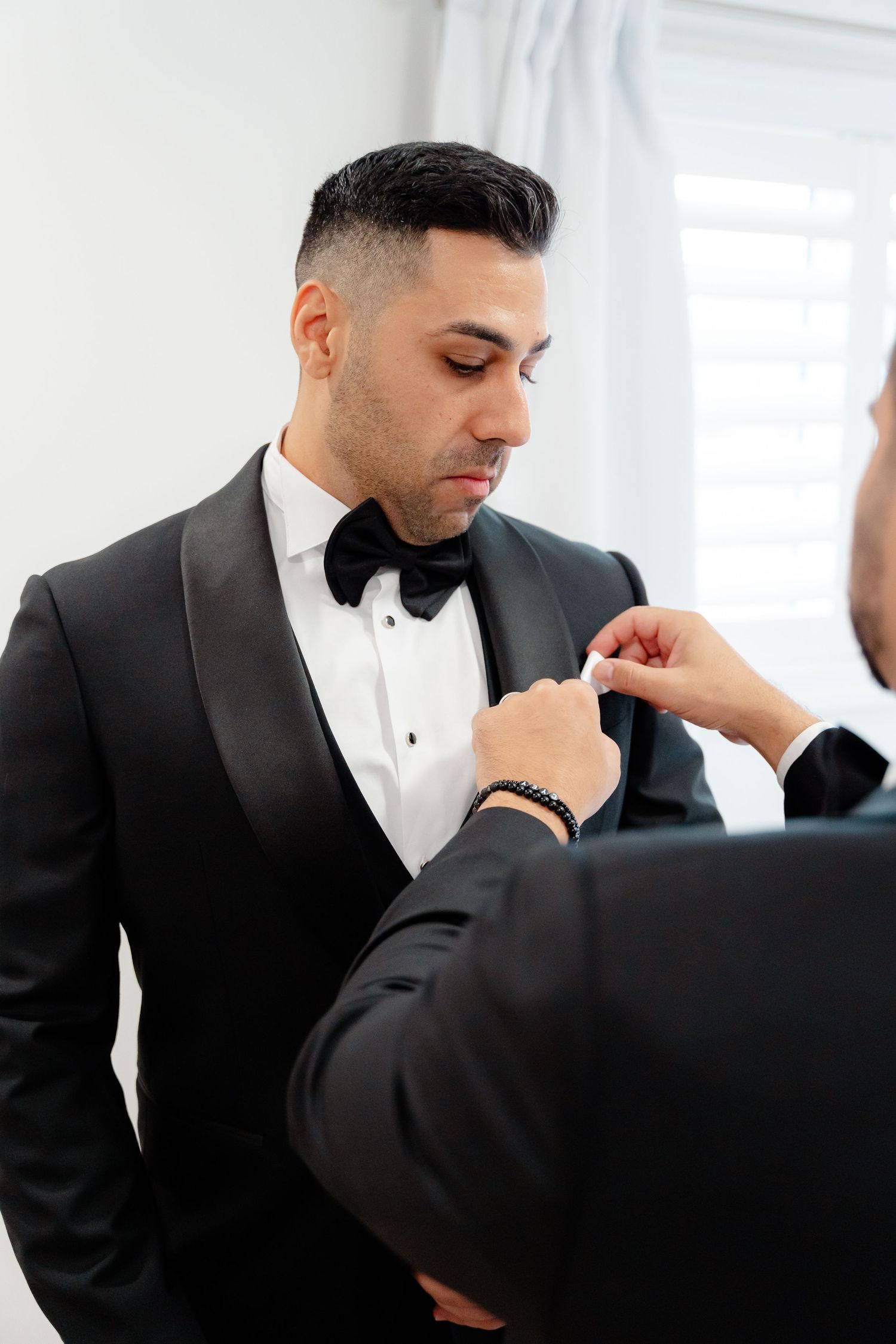Someone adjusts a black bowtie on a formal tuxedo during pre-wedding preparations.