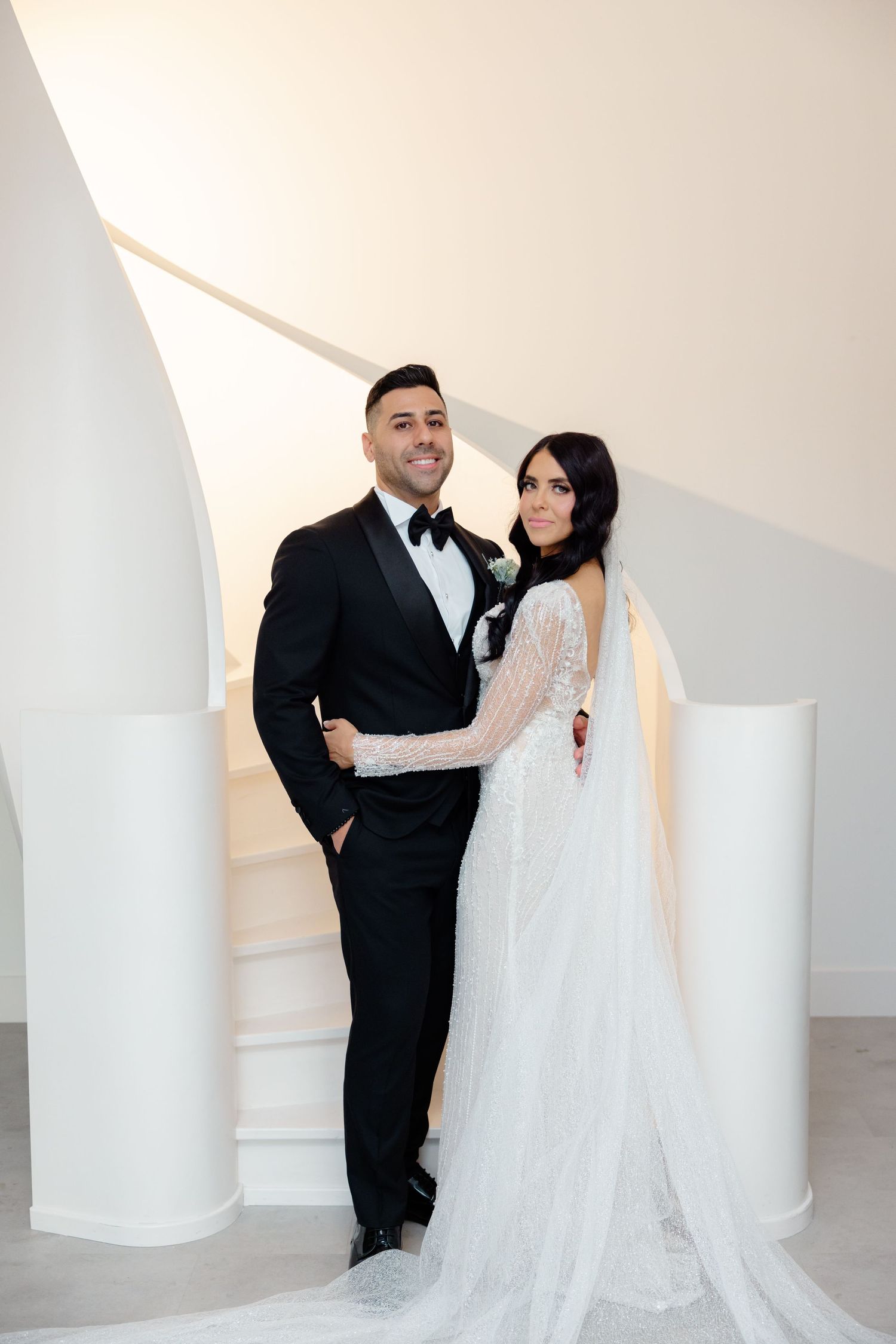 Elegant wedding couple posing on stairs with modern white architectural elements.